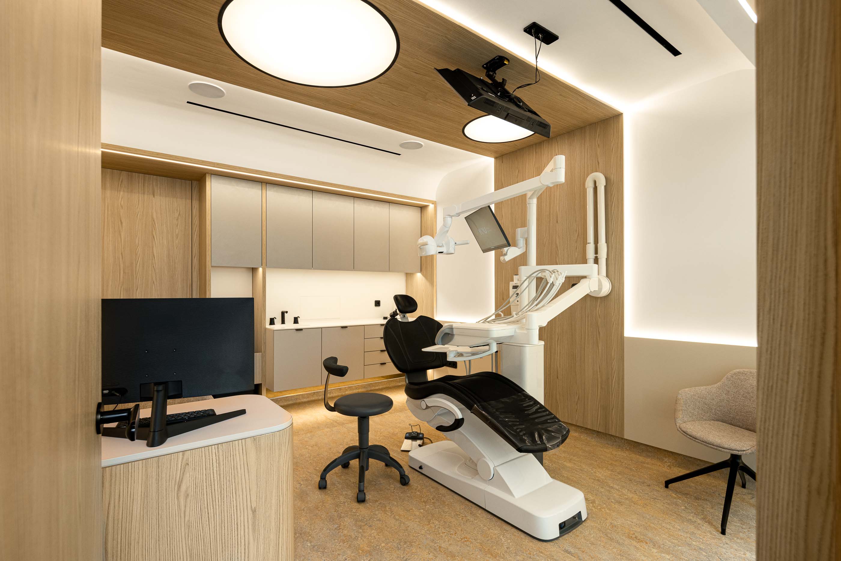 Gabinete: Equipamento dentário moderno, cadeira ergonómica e secretária de apoio num ambiente luminoso. — YOU – Clínica Dentária arquitetura Radian Contemporary Architecture em Malveira