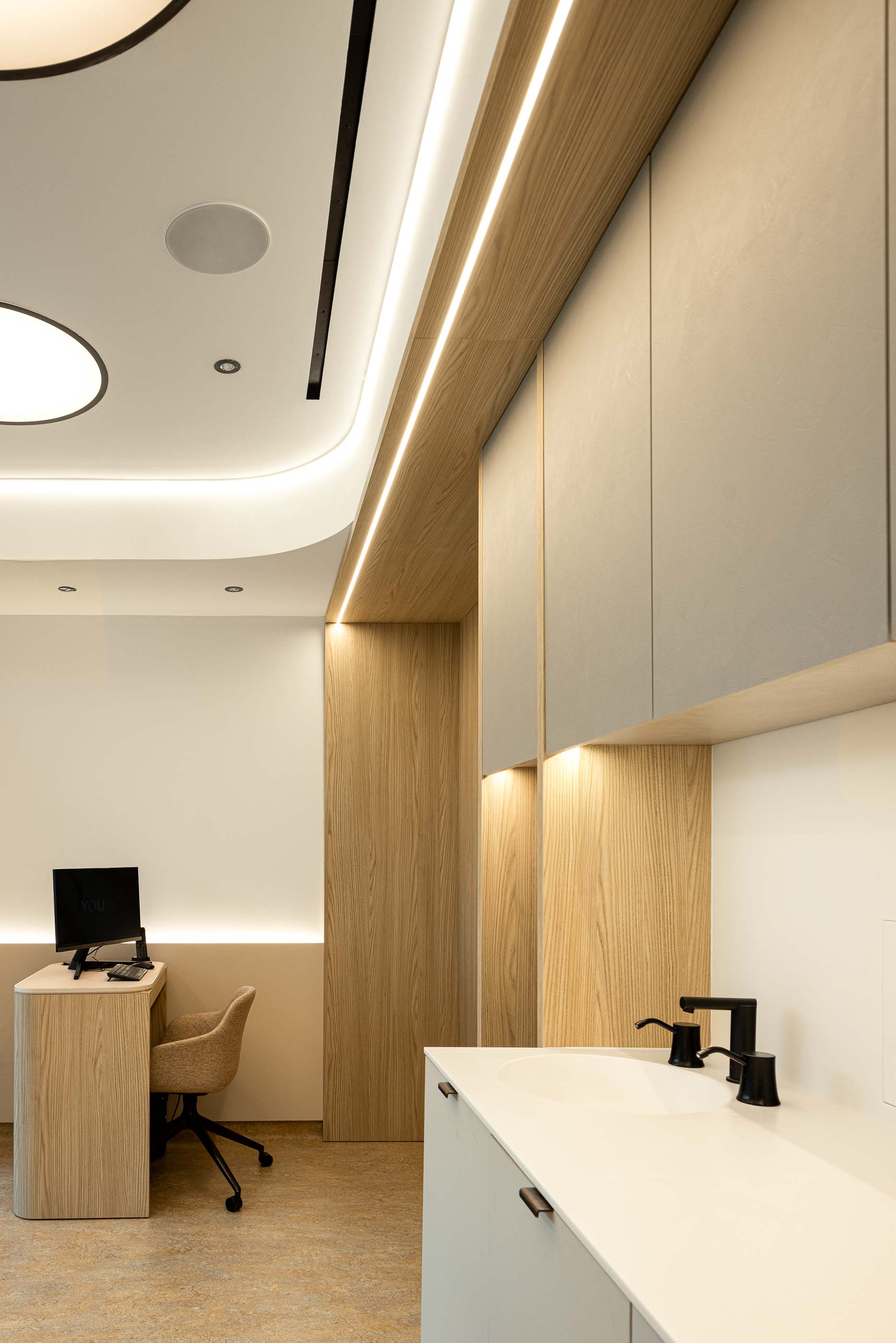 Gabinete: Secretária de apoio com computador, lavatório e armários embutidos, com iluminação indireta. — YOU – Clínica Dentária arquitetura Radian Contemporary Architecture em Malveira