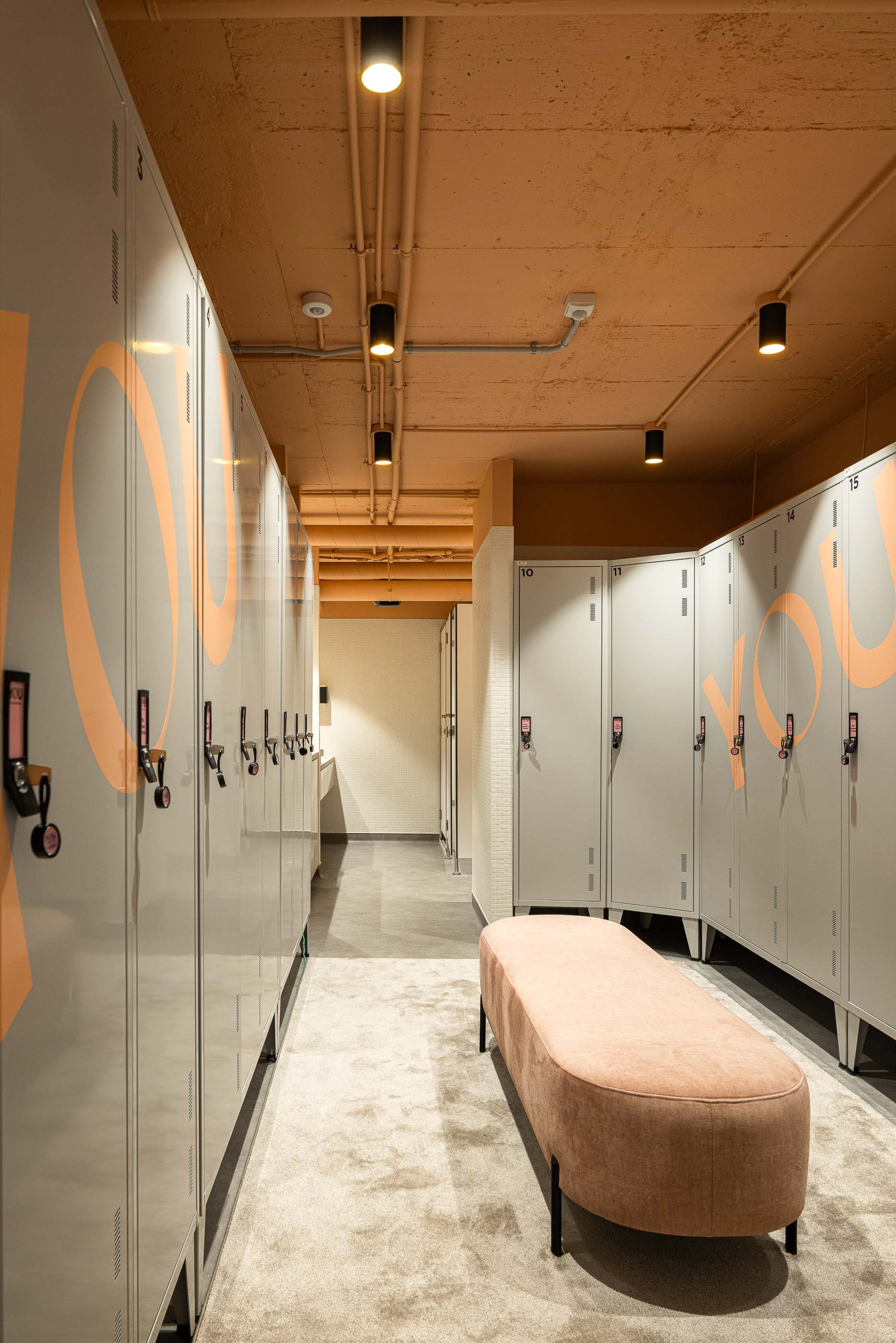 Balneário: Cacifos com o logótipo da clínica, banco almofadado e iluminação pontual no teto. — YOU – Clínica Dentária arquitetura Radian Contemporary Architecture em Malveira