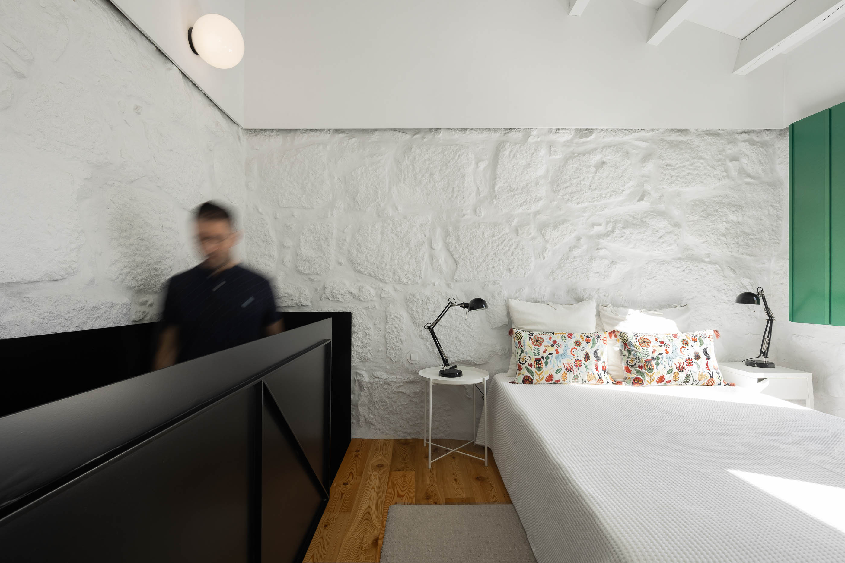 Quarto: Vista geral da cama, mesas de cabeceira, parede em pedra branca e guarda-corpo preto. Pavimento em madeira clara. — Casa Covelo arquitetura spaceworkers em Porto