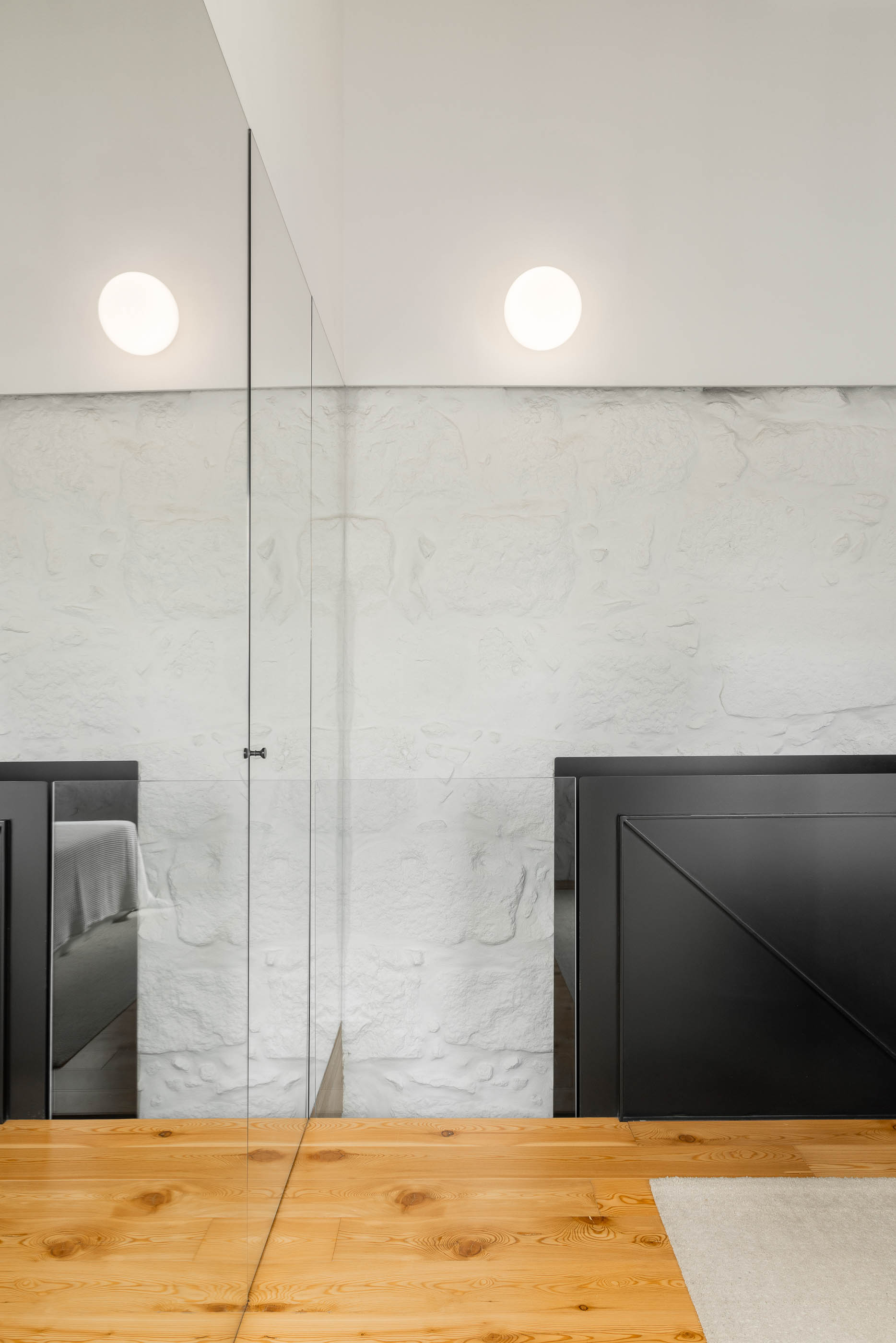 Quarto: Detalhe do espelho amplo, guarda-roupa preto e pavimento em madeira clara. Parede em pedra branca. — Casa Covelo arquitetura spaceworkers em Porto