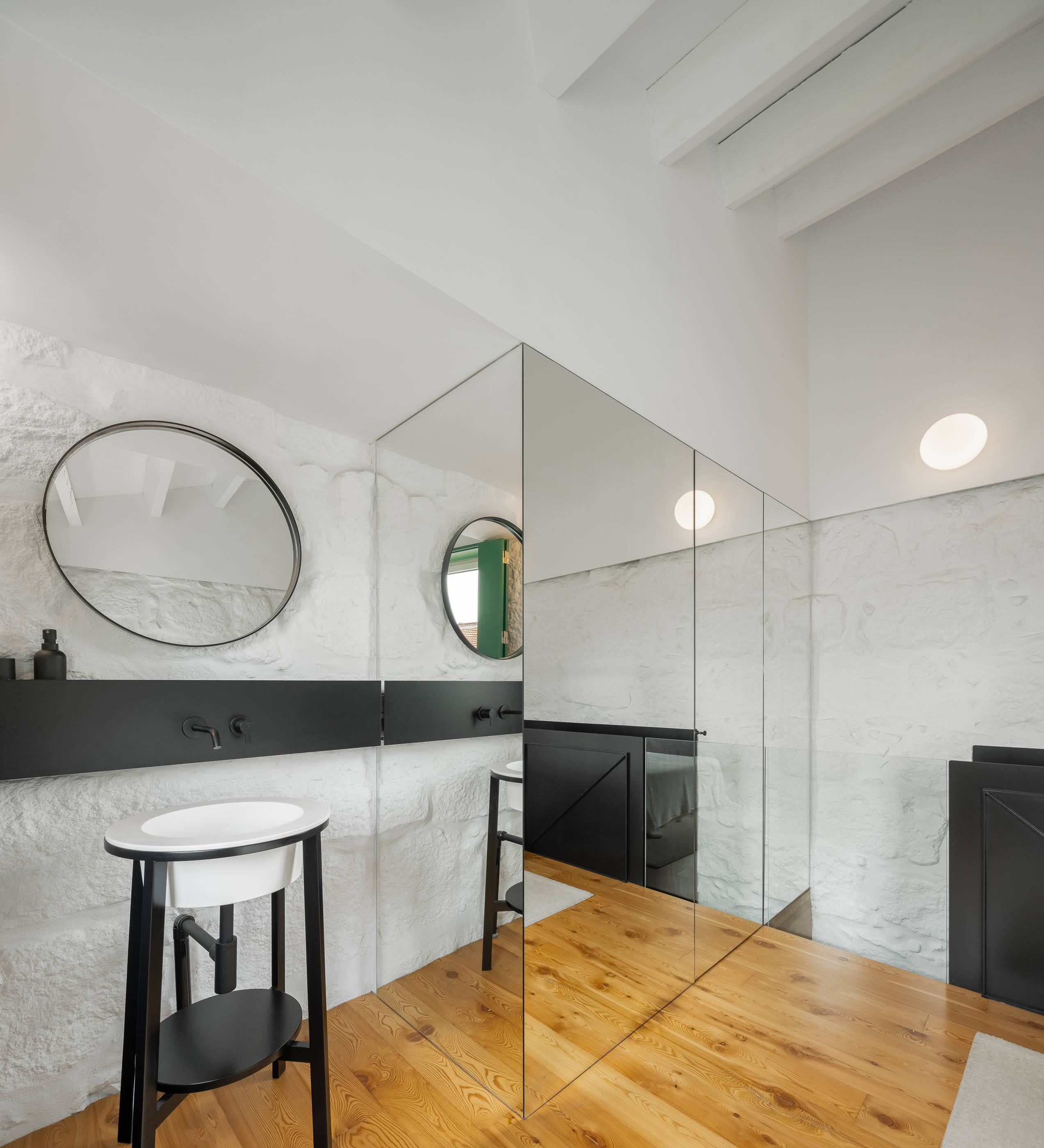 Casa de banho: Espelho amplo, lavatório branco, parede em pedra branca e pavimento em madeira clara. — Casa Covelo arquitetura spaceworkers em Porto