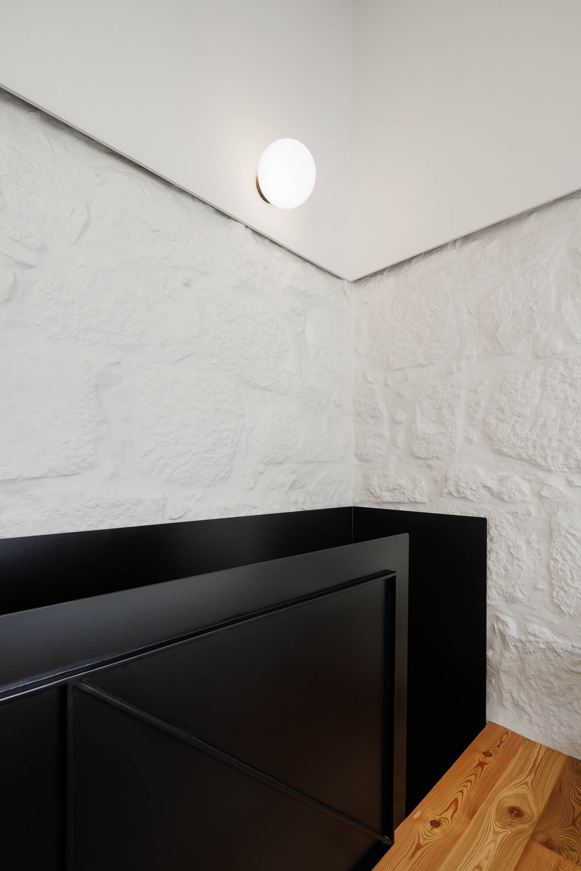 Quarto: Detalhe do guarda-corpo preto com padrão geométrico e parede em pedra branca. Pavimento em madeira clara. — Casa Covelo arquitetura spaceworkers em Porto