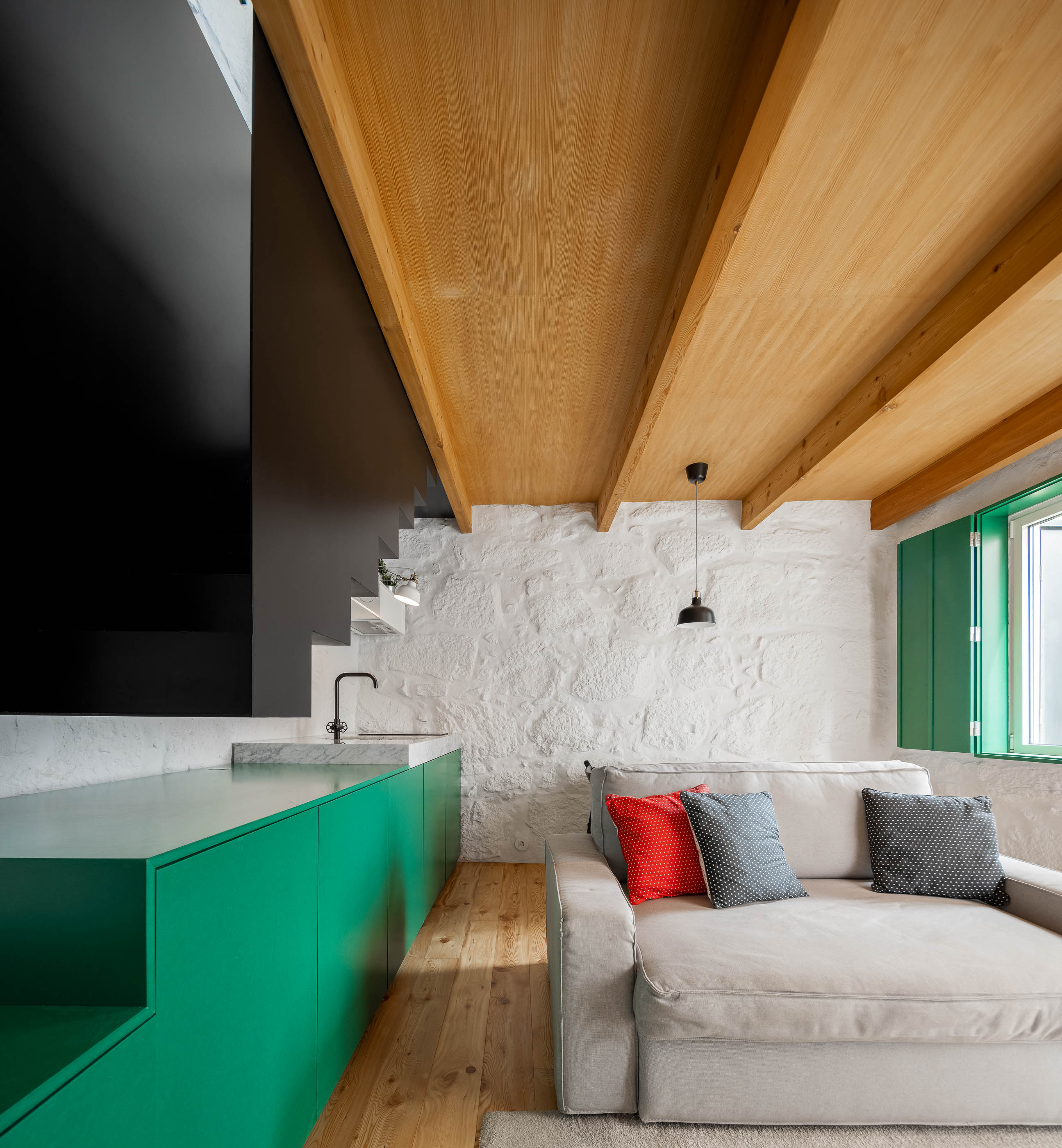 Sala de estar/Escada: Escada preta, bancada verde, parede em pedra branca e teto em madeira. Sofá cinzento. — Casa Covelo arquitetura spaceworkers em Porto