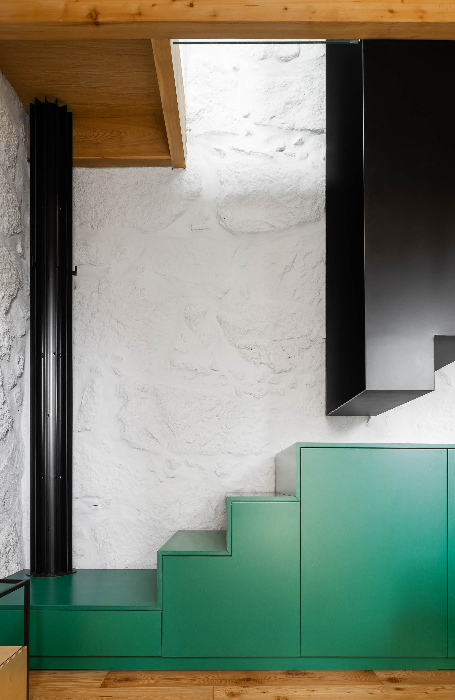 Sala de estar/Escada: Escada preta, bancada verde e parede em pedra branca. Teto em madeira. — Casa Covelo arquitetura spaceworkers em Porto