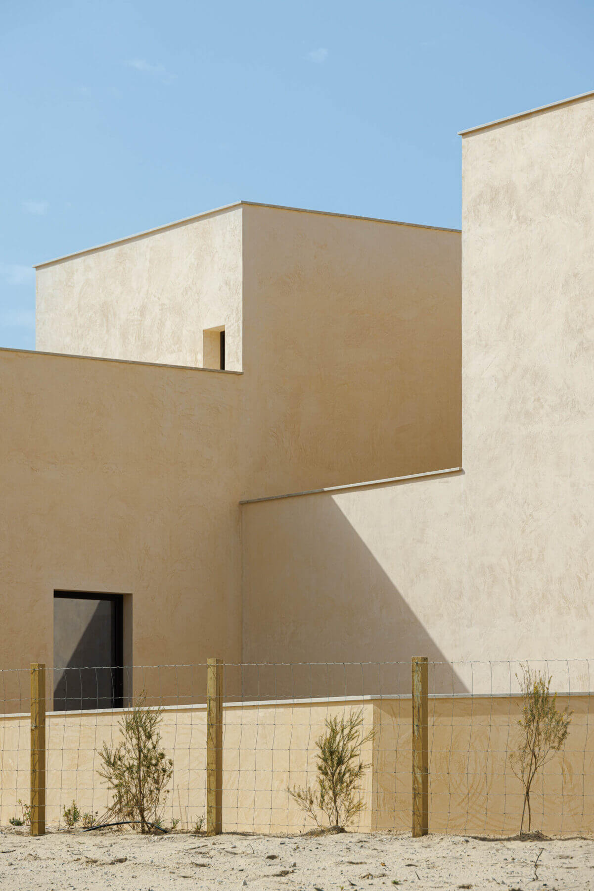 Exterior: Fachada minimalista com acabamento texturado bege, janelas escuras e vedação rústica. — Parada das Estrelas arquitetura Solano Soto Architecture Studio em Óbidos