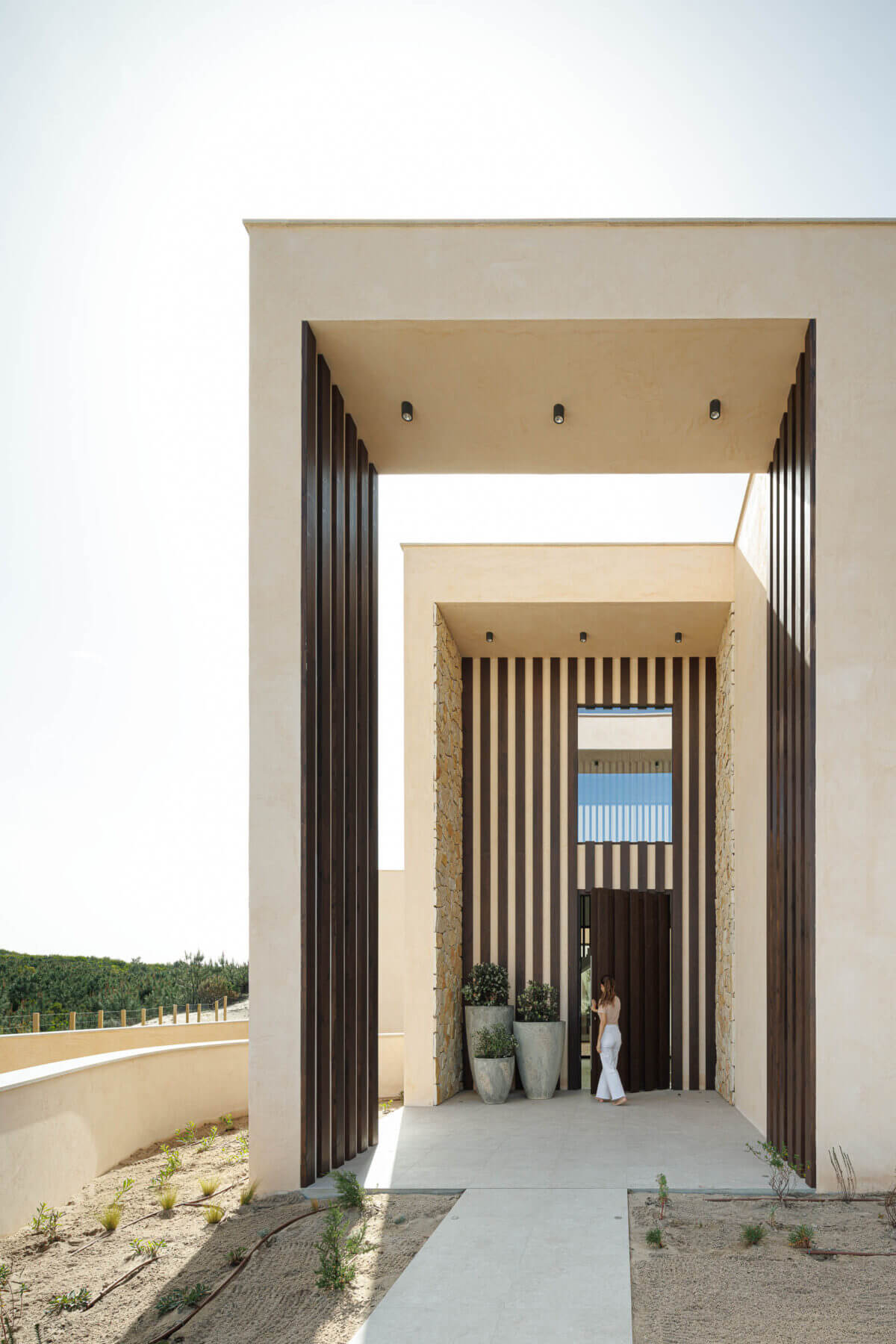 Entrada: Alpendre com colunas verticais de madeira, vasos com plantas e pavimento em betão. — Parada das Estrelas arquitetura Solano Soto Architecture Studio em Óbidos
