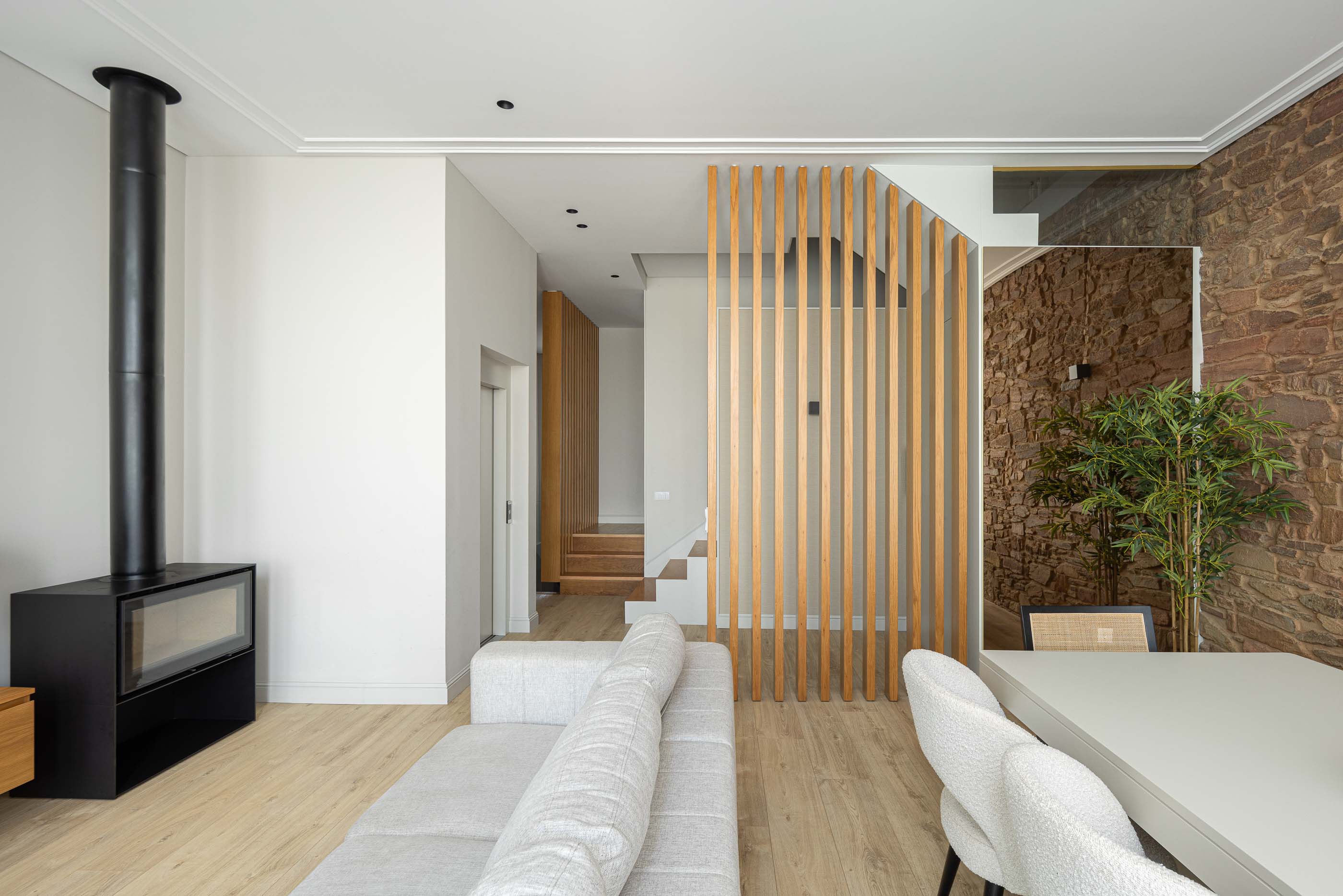 Sala de estar: Sala com lareira preta, sofá cinzento, mesa de jantar branca e parede em pedra. — Casa do Parque IV arquitetura Ricardo Azevedo Arquitecto em Santo Tirso