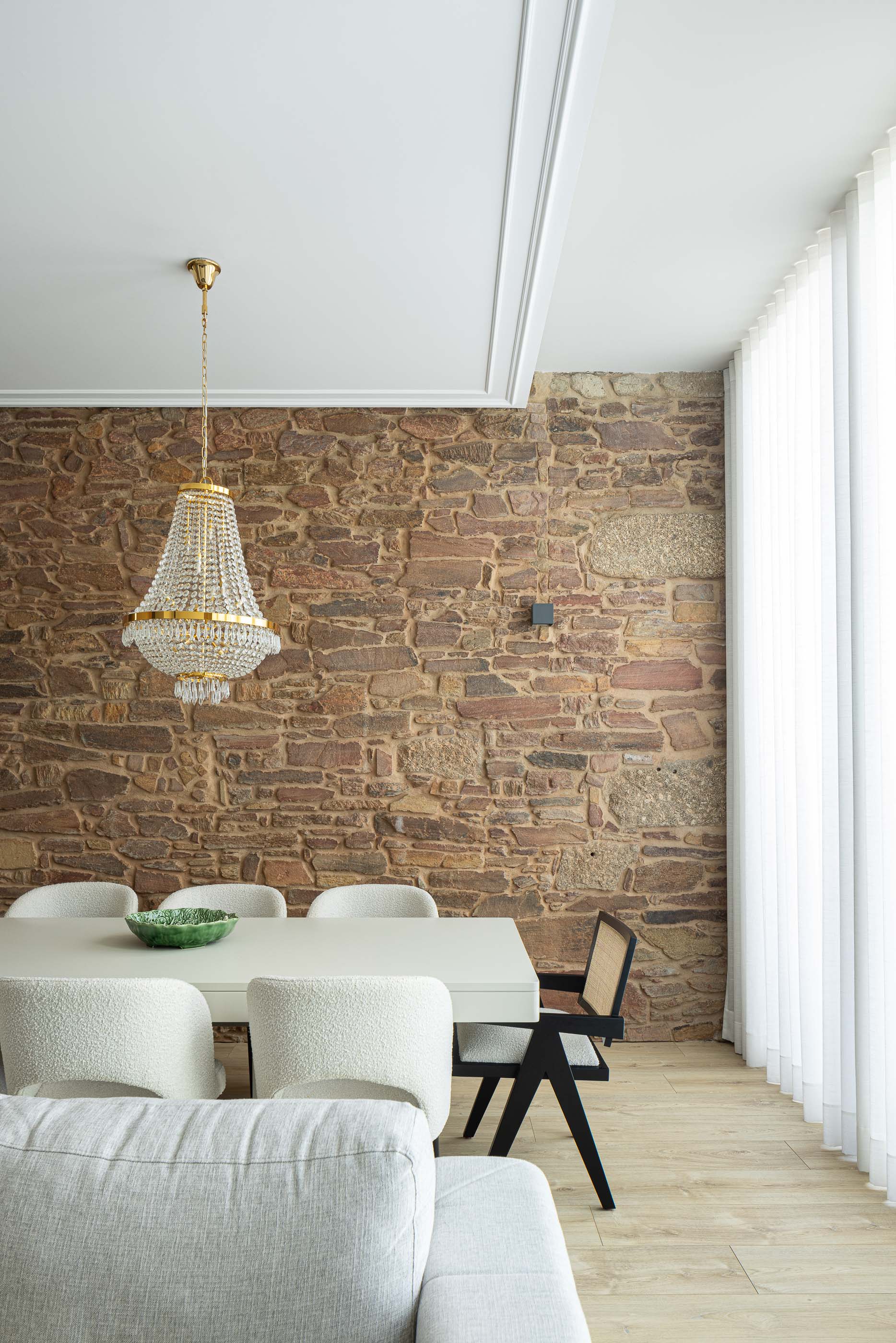 Sala de jantar: Mesa de jantar branca com cadeiras e candeeiro clássico, em frente a parede de pedra. — Casa do Parque IV arquitetura Ricardo Azevedo Arquitecto em Santo Tirso