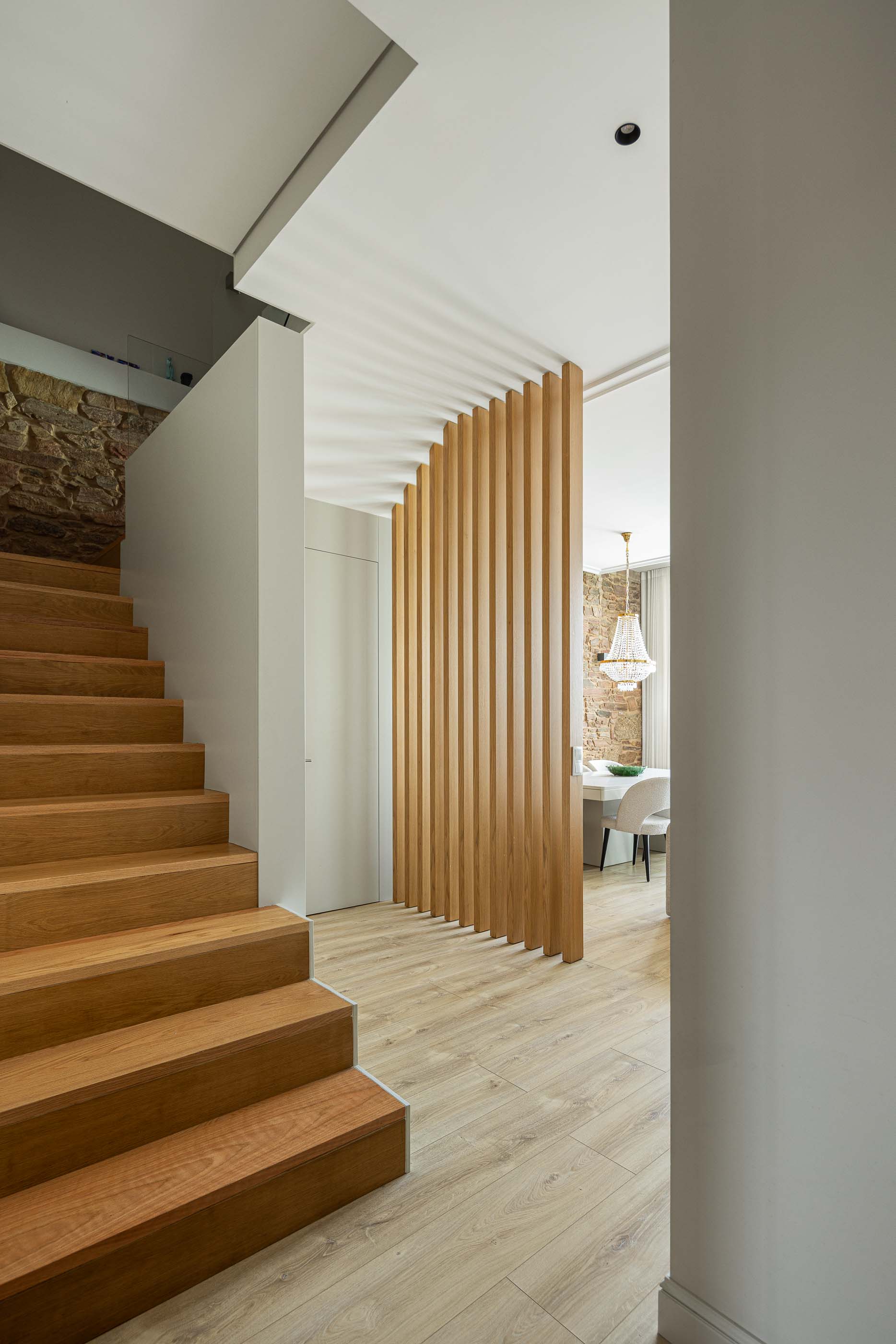 Escadas: Escadas em madeira com parede em pedra, painel vertical em madeira e vista para a sala de jantar. — Casa do Parque IV arquitetura Ricardo Azevedo Arquitecto em Santo Tirso
