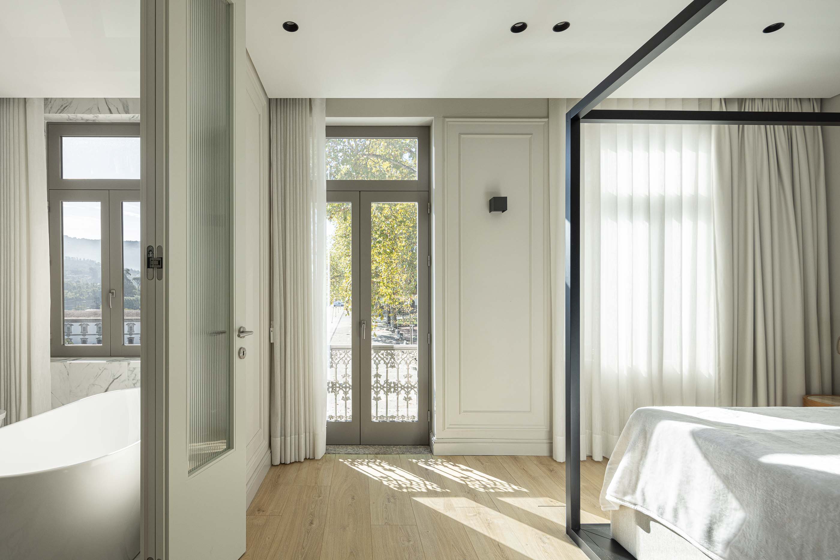 Quarto: Quarto com cama de dossel preta, pavimento em madeira e acesso à varanda com vista panorâmica. — Casa do Parque IV arquitetura Ricardo Azevedo Arquitecto em Santo Tirso