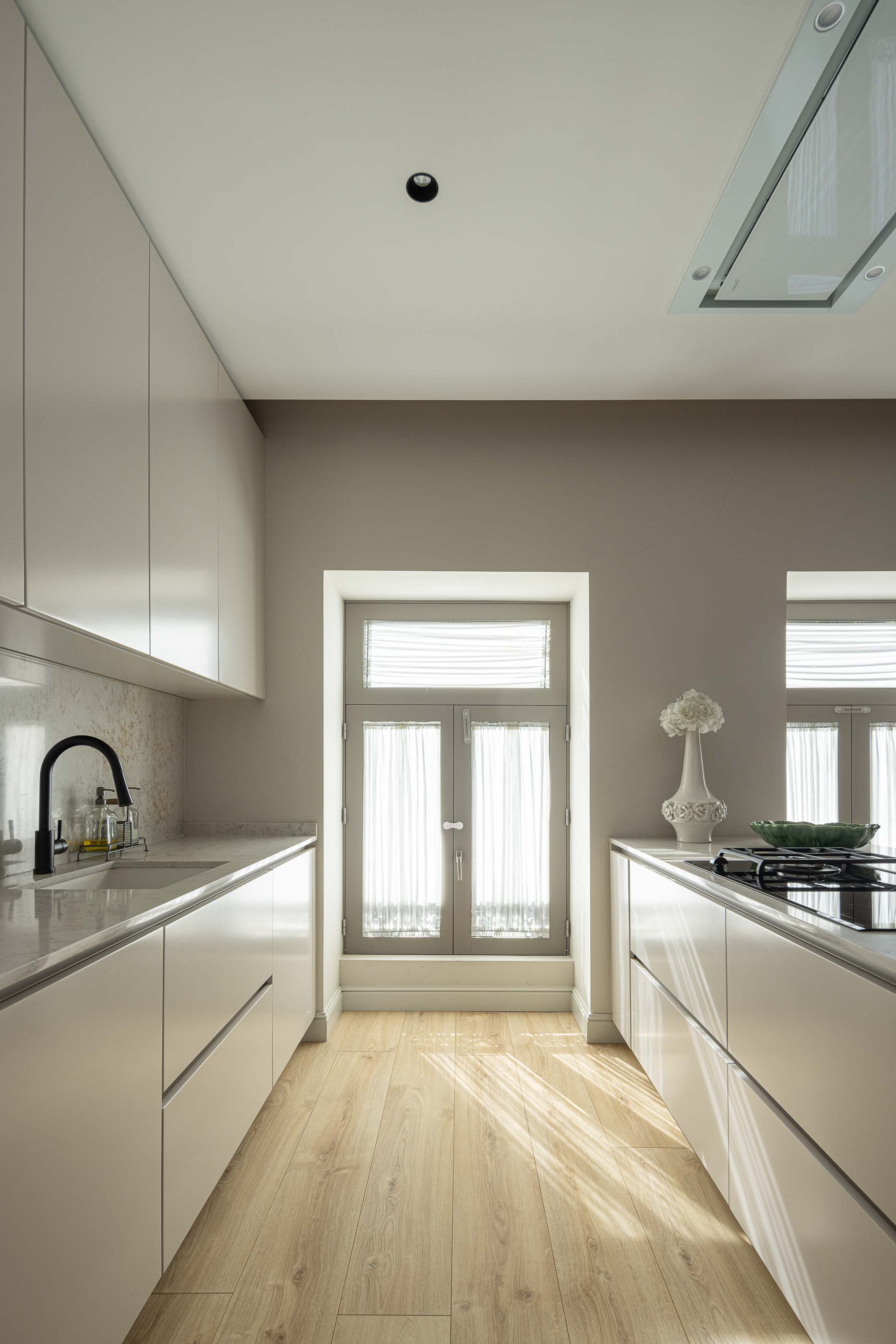 Cozinha: Cozinha minimalista com armários brancos, bancada em pedra clara e pavimento em madeira. — Casa do Parque IV arquitetura Ricardo Azevedo Arquitecto em Santo Tirso