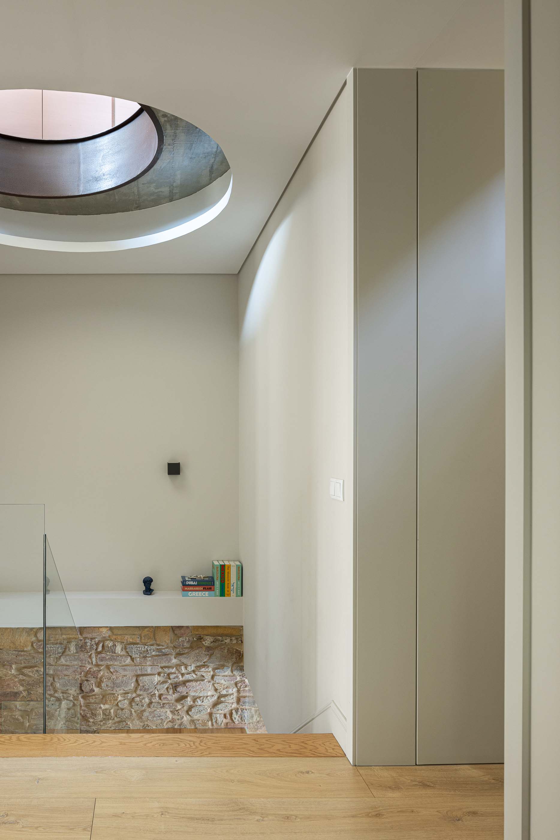 Escadas: Vista das escadas em madeira com clarabóia circular e parede em pedra exposta. — Casa do Parque IV arquitetura Ricardo Azevedo Arquitecto em Santo Tirso