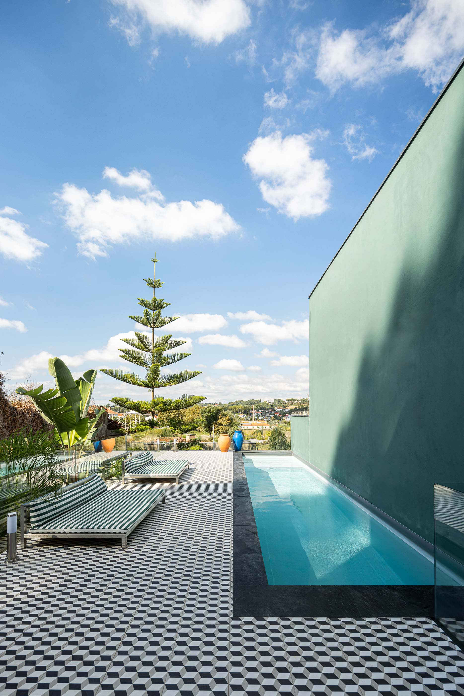 Exterior: Vista da piscina com espreguiçadeiras, pavimento geométrico e parede verde. — Casa do Parque IV arquitetura Ricardo Azevedo Arquitecto em Santo Tirso