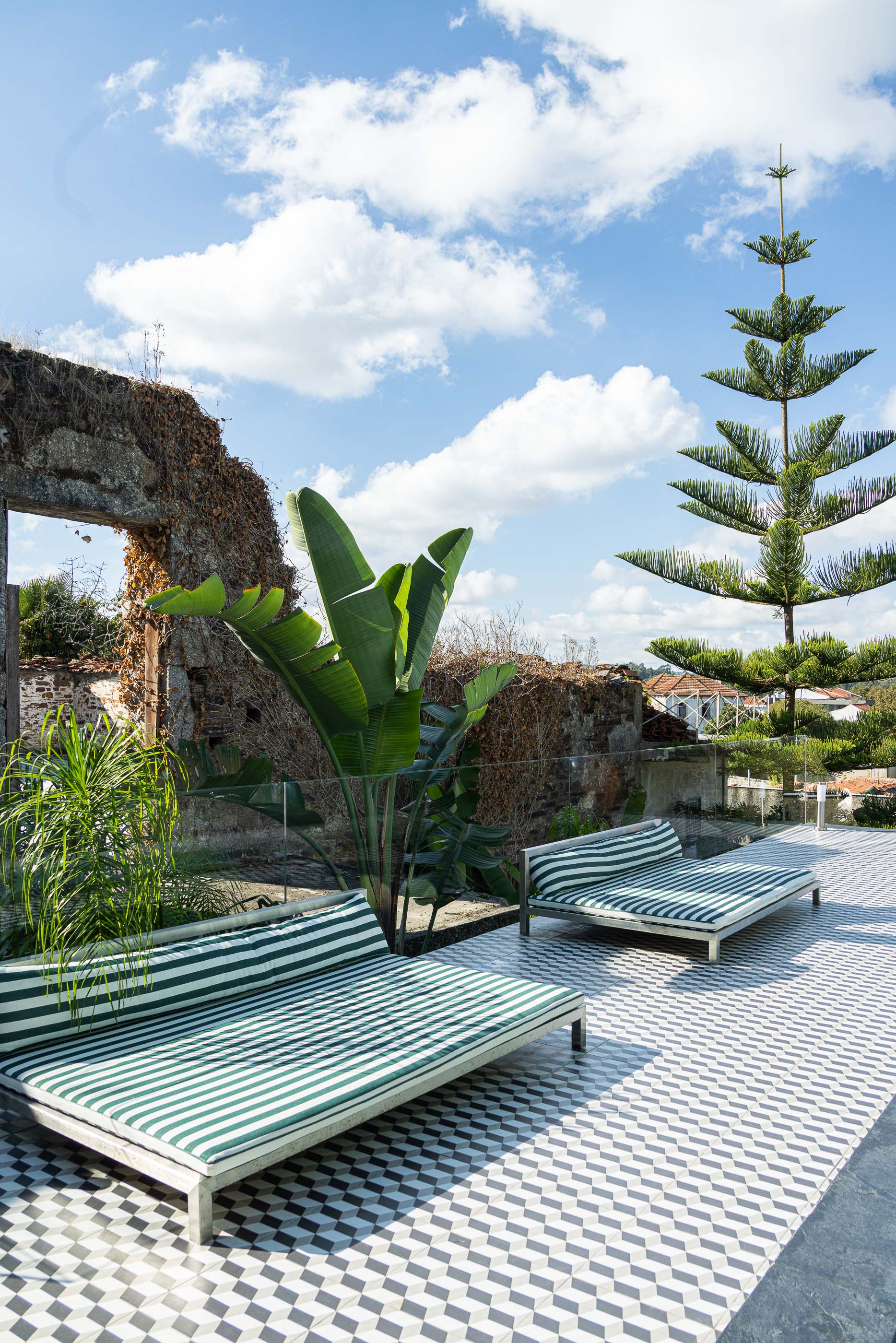Exterior: Espreguiçadeiras com almofadas às riscas e ruínas em pedra ao fundo. — Casa do Parque IV arquitetura Ricardo Azevedo Arquitecto em Santo Tirso