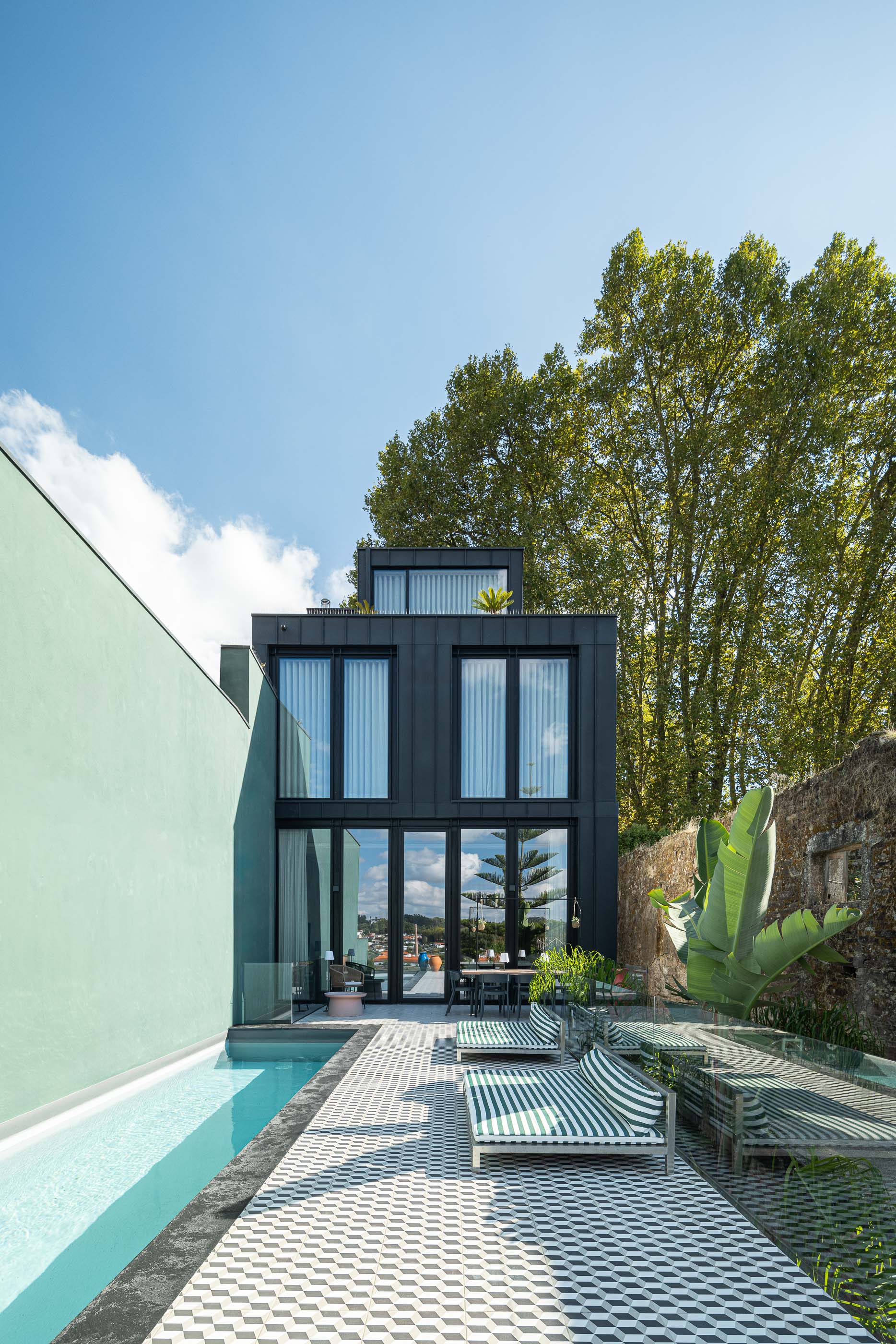 Exterior: Fachada posterior da casa com piscina, espreguiçadeiras e detalhes em verde. — Casa do Parque IV arquitetura Ricardo Azevedo Arquitecto em Santo Tirso