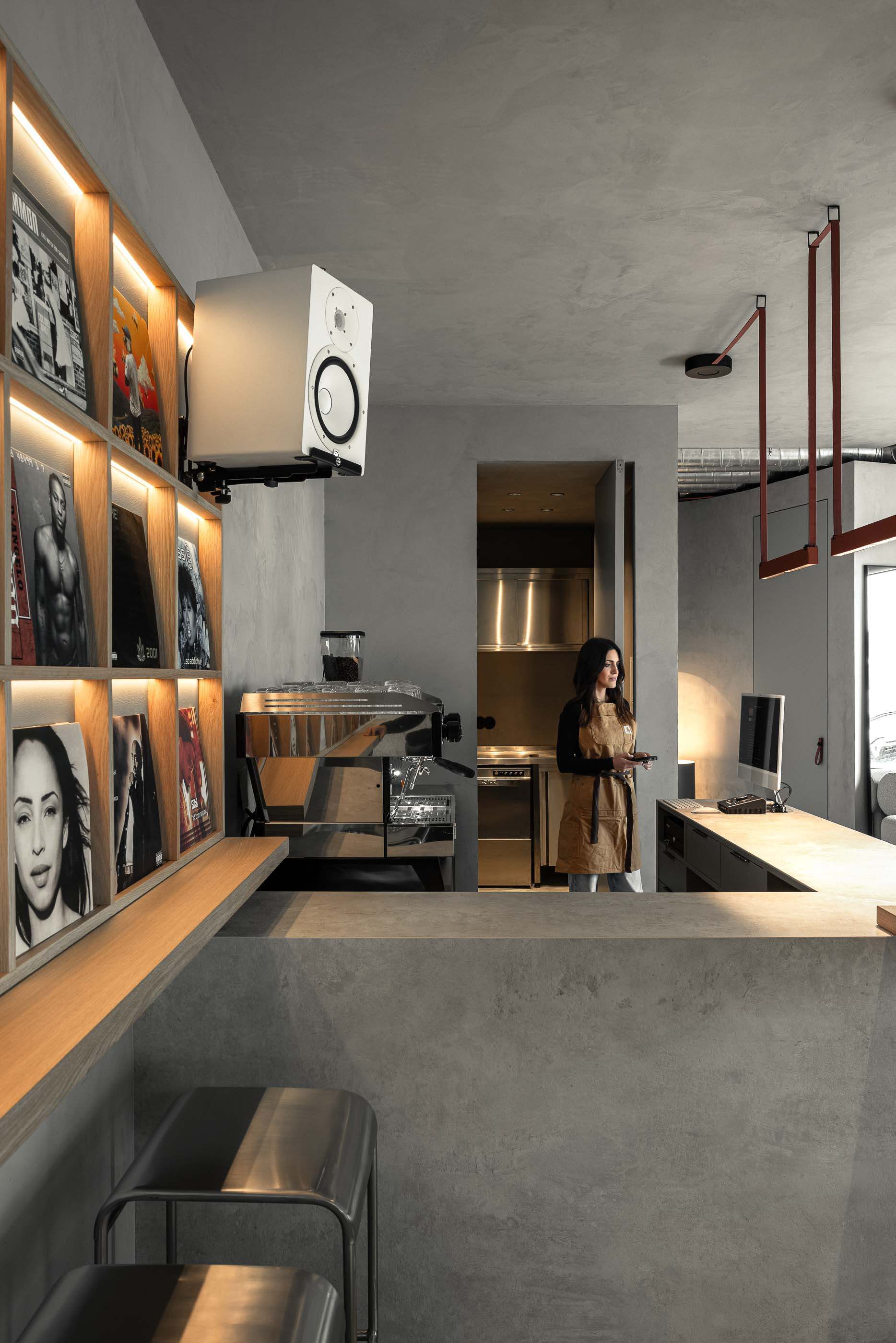 Balcão: Balcão de betão cinzento com máquina de café, estante de discos iluminada e candeeiros suspensos. — KI.art.music.coffee arquitetura MAT Arquitetura e Interiores em Porto