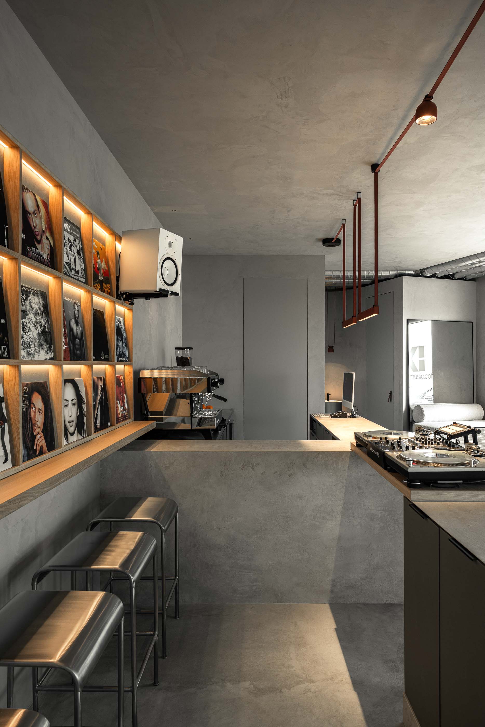 Balcão: Balcão de betão cinzento com gira-discos, estante de discos iluminada e pavimento cinzento. — KI.art.music.coffee arquitetura MAT Arquitetura e Interiores em Porto