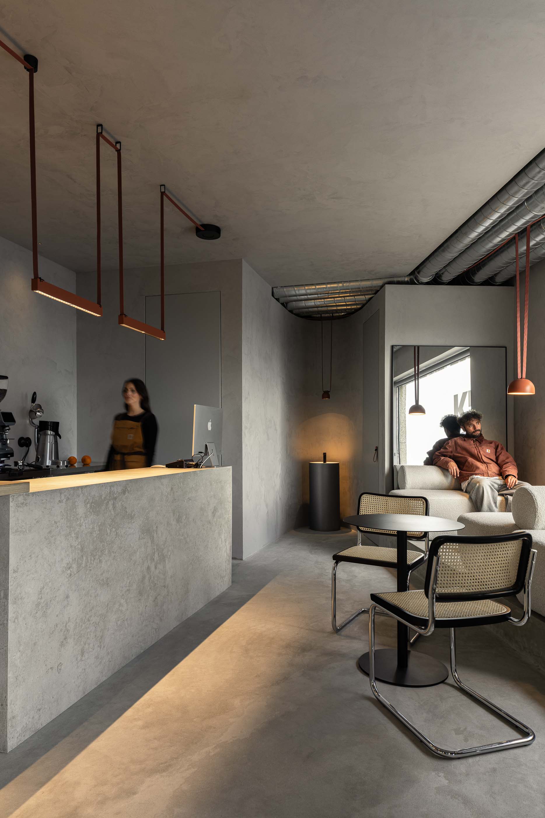 Espaço de mesas: Balcão de betão, sofás brancos, cadeiras de palhinha e candeeiros suspensos em espaço com pavimento cinzento. — KI.art.music.coffee arquitetura MAT Arquitetura e Interiores em Porto