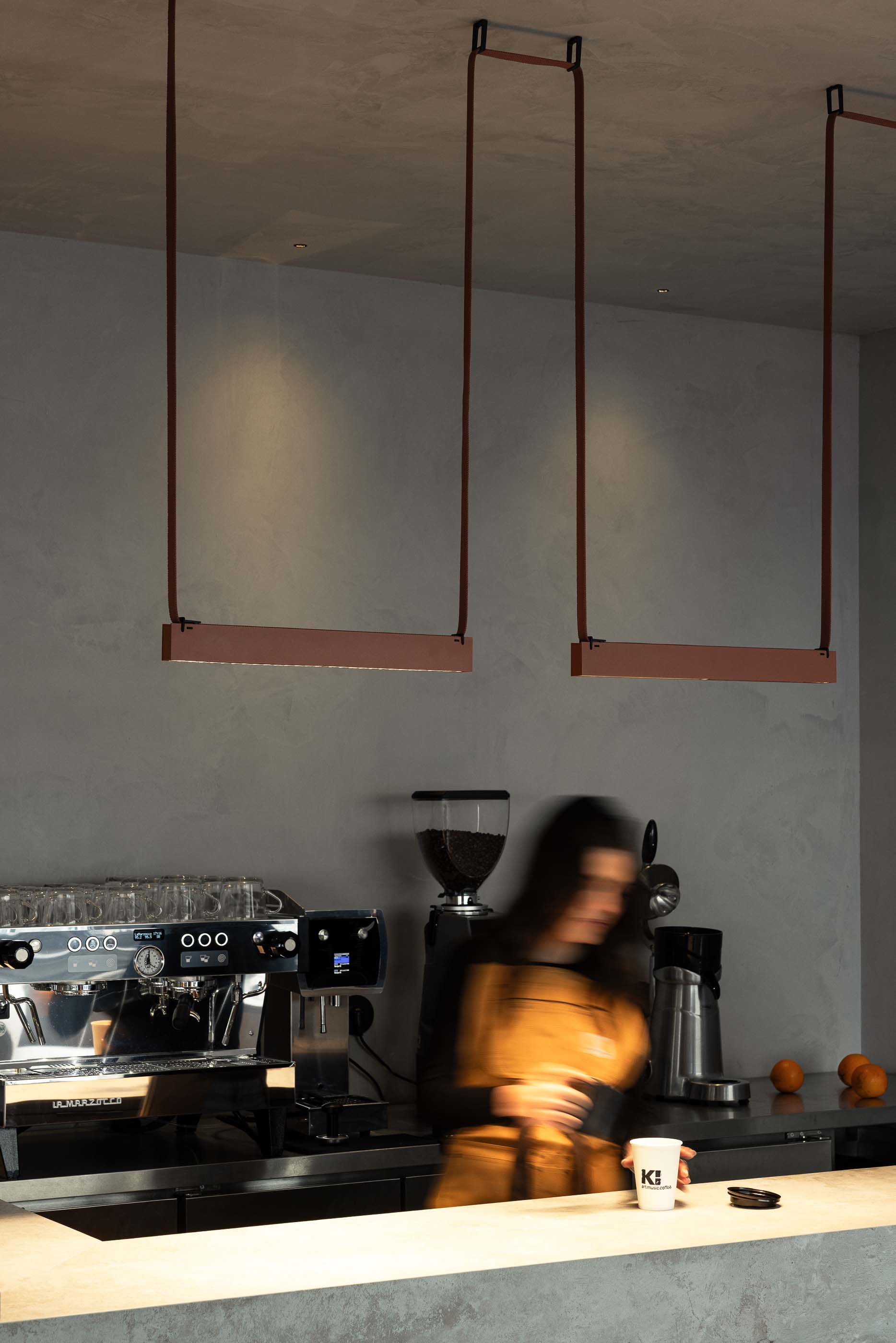 Balcão: Detalhe da máquina de café sobre o balcão cinzento com candeeiros suspensos e parede texturada. — KI.art.music.coffee arquitetura MAT Arquitetura e Interiores em Porto