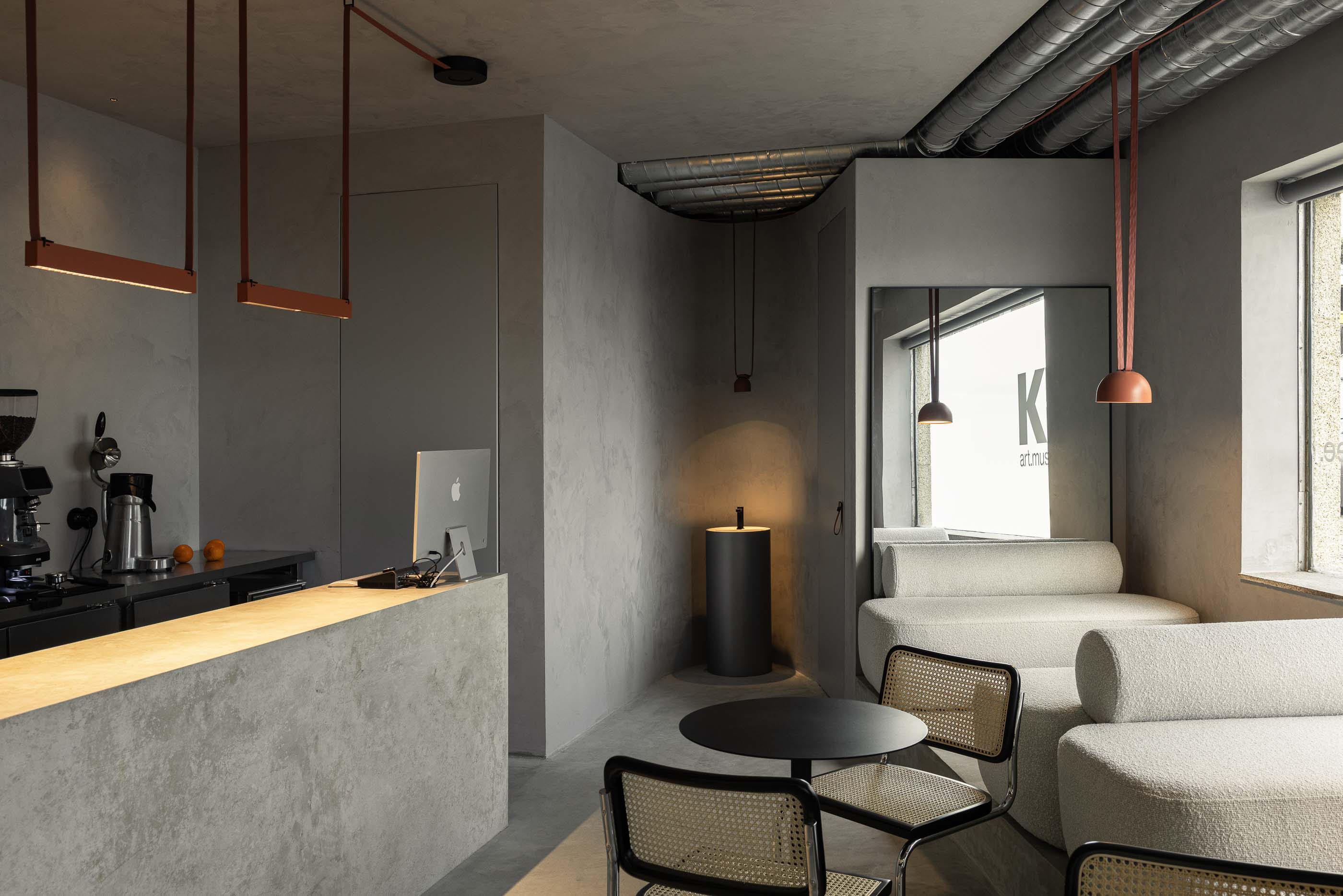 Perspectiva geral: Balcão de betão, sofás brancos, cadeiras de palhinha, candeeiros suspensos e tubagens expostas no tecto. — KI.art.music.coffee arquitetura MAT Arquitetura e Interiores em Porto