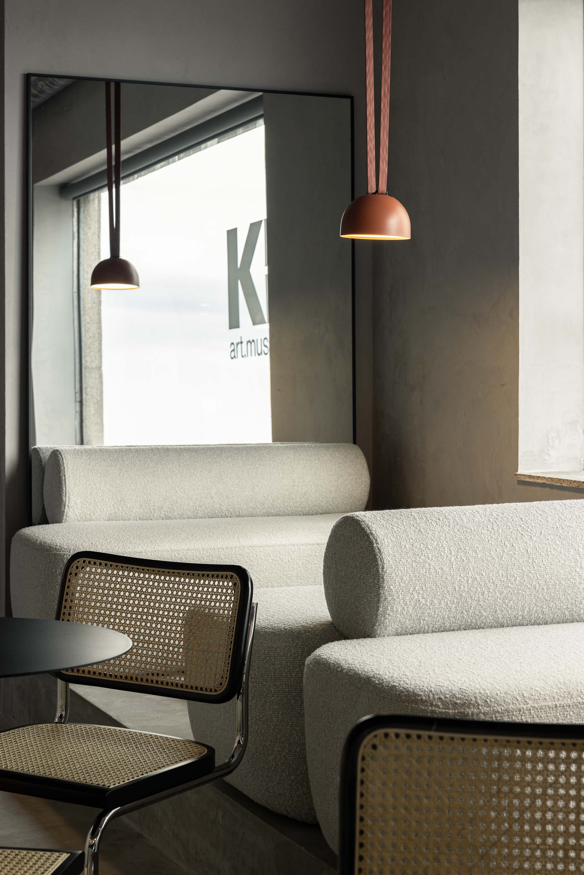 Zona de sofás: Sofá branco com candeeiro suspenso e espelho, cadeiras de palhinha e pavimento cinzento. — KI.art.music.coffee arquitetura MAT Arquitetura e Interiores em Porto