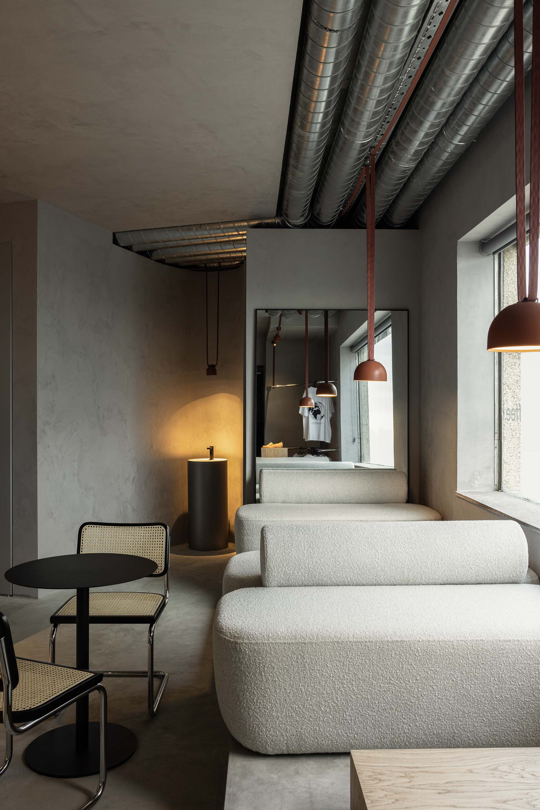 Zona de sofás: Sofás brancos, cadeiras de palhinha, candeeiro suspenso e lavatório cilíndrico em espaço com tubagens expostas. — KI.art.music.coffee arquitetura MAT Arquitetura e Interiores em Porto