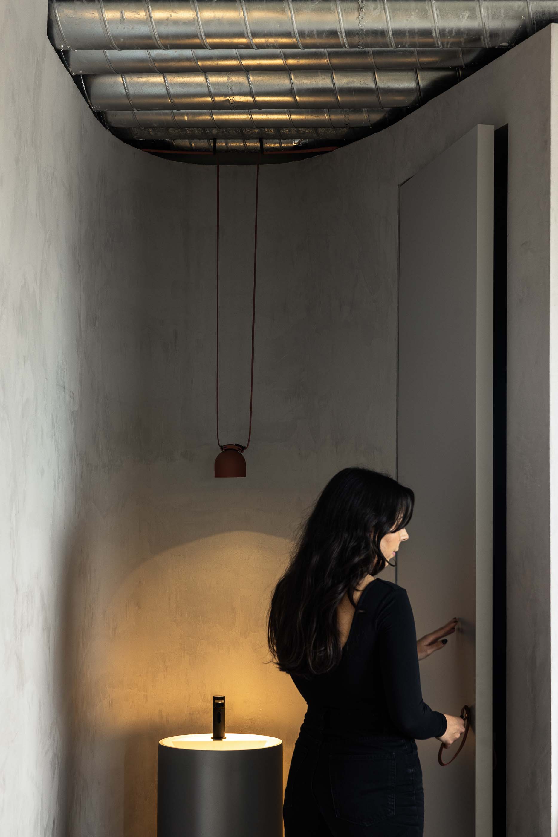 Casa de banho: Lavatório cilíndrico preto, candeeiro suspenso e porta branca em espaço com parede texturada. — KI.art.music.coffee arquitetura MAT Arquitetura e Interiores em Porto