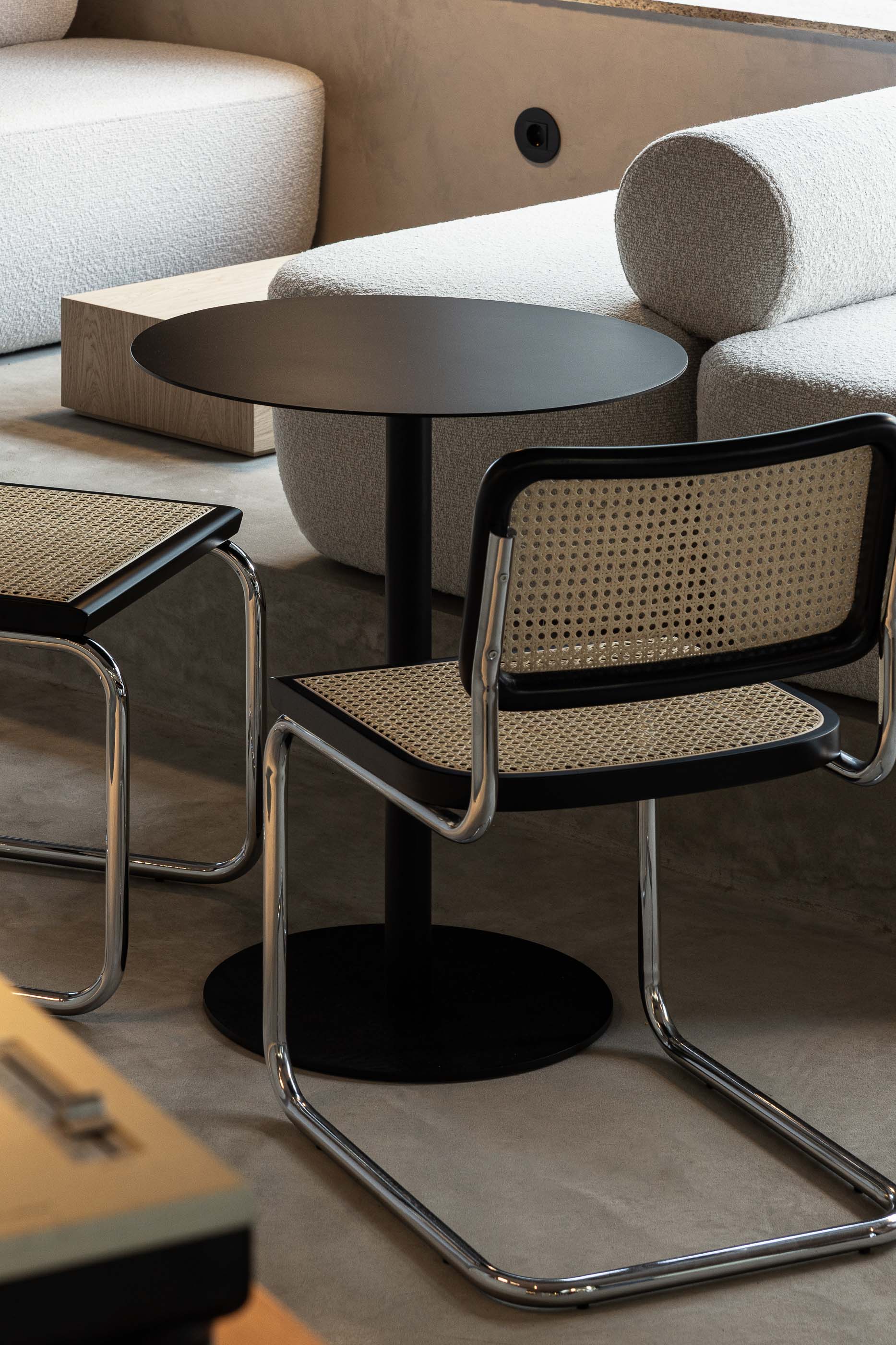 Detalhe da zona de sofás: Cadeira de palhinha, mesa preta e sofá branco em espaço com pavimento cinzento. — KI.art.music.coffee arquitetura MAT Arquitetura e Interiores em Porto