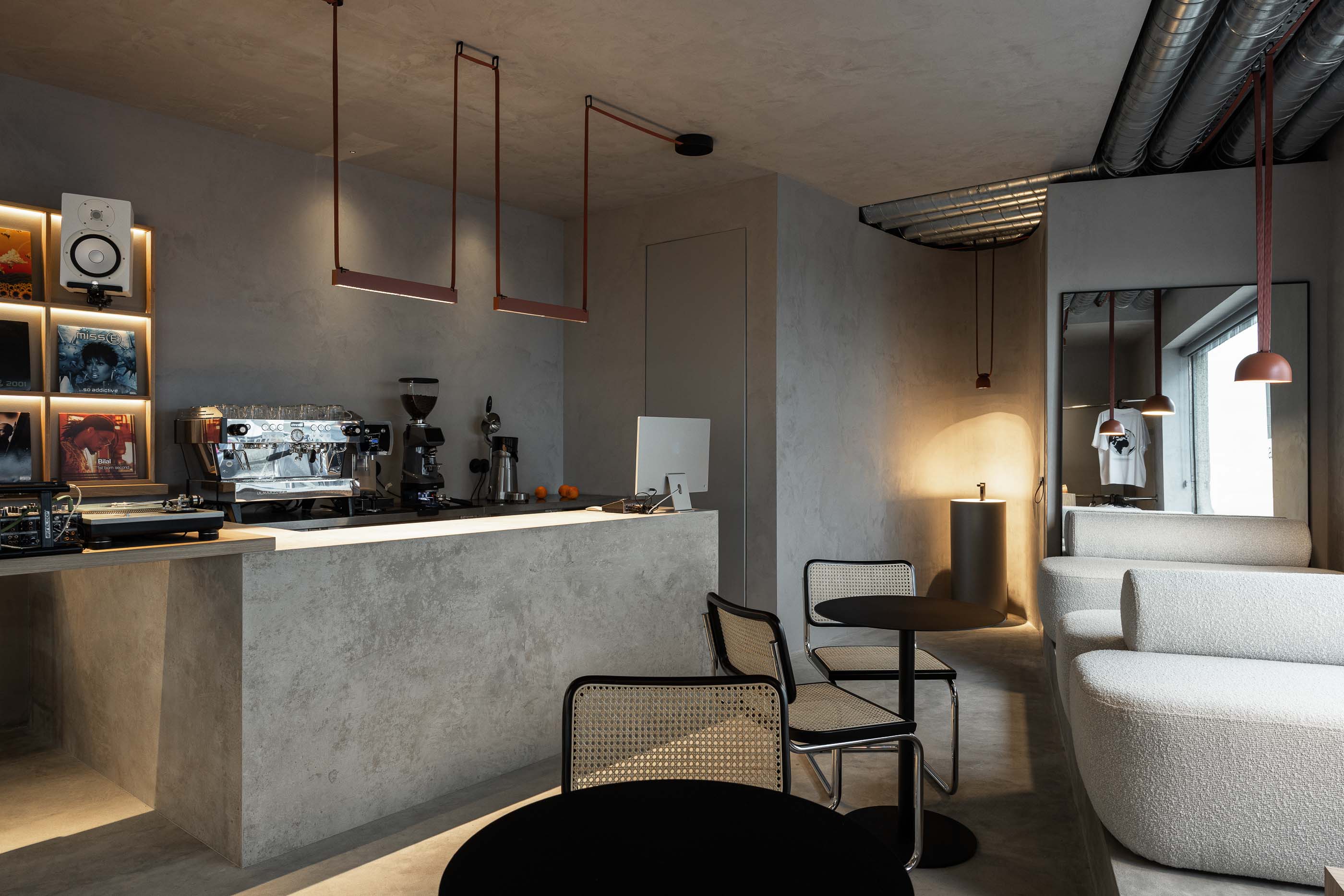 Perspectiva geral: Balcão de betão, estante de discos, sofás brancos, cadeiras de palhinha e candeeiros suspensos. — KI.art.music.coffee arquitetura MAT Arquitetura e Interiores em Porto