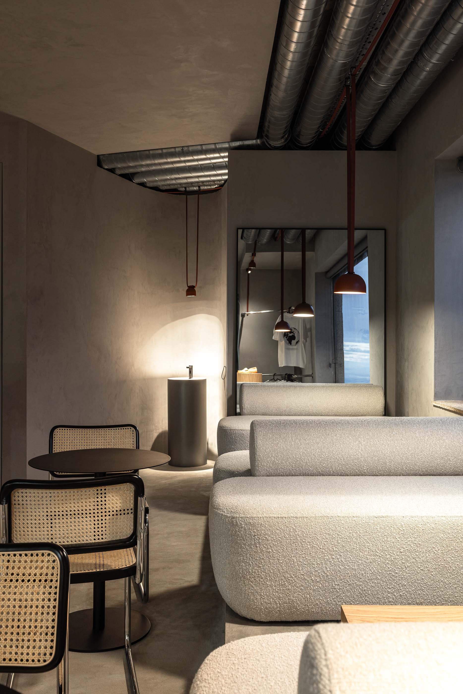 Perspectiva geral: Sofás brancos, cadeiras de palhinha, lavatório cilíndrico e candeeiros suspensos em espaço cinzento. — KI.art.music.coffee arquitetura MAT Arquitetura e Interiores em Porto