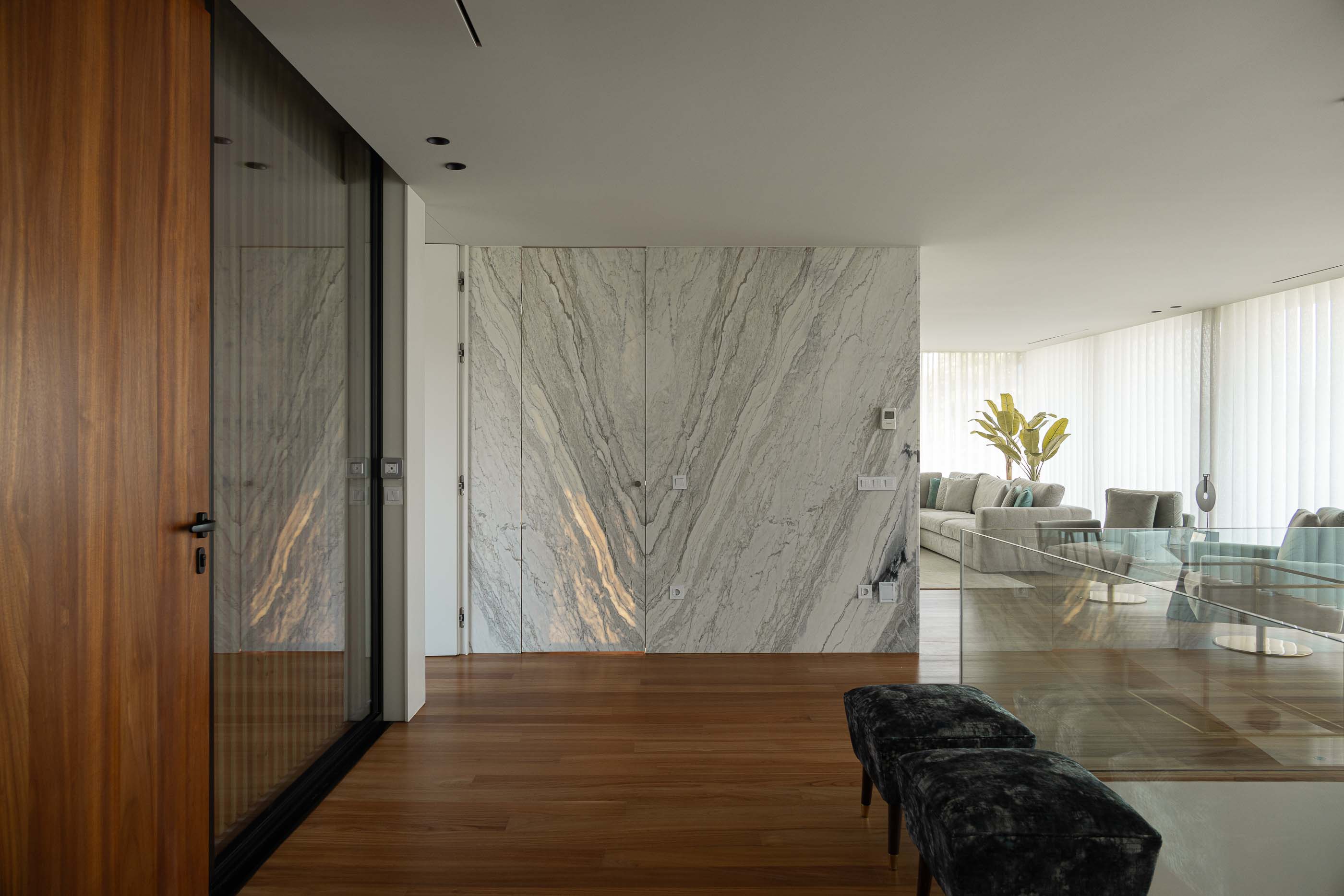 Hall de entrada: Hall com pavimento em madeira, porta em madeira escura, divisória em mármore e vista para a sala de estar. — Casa da Encosta arquitetura Ricardo Azevedo Arquitecto em Santo Tirso