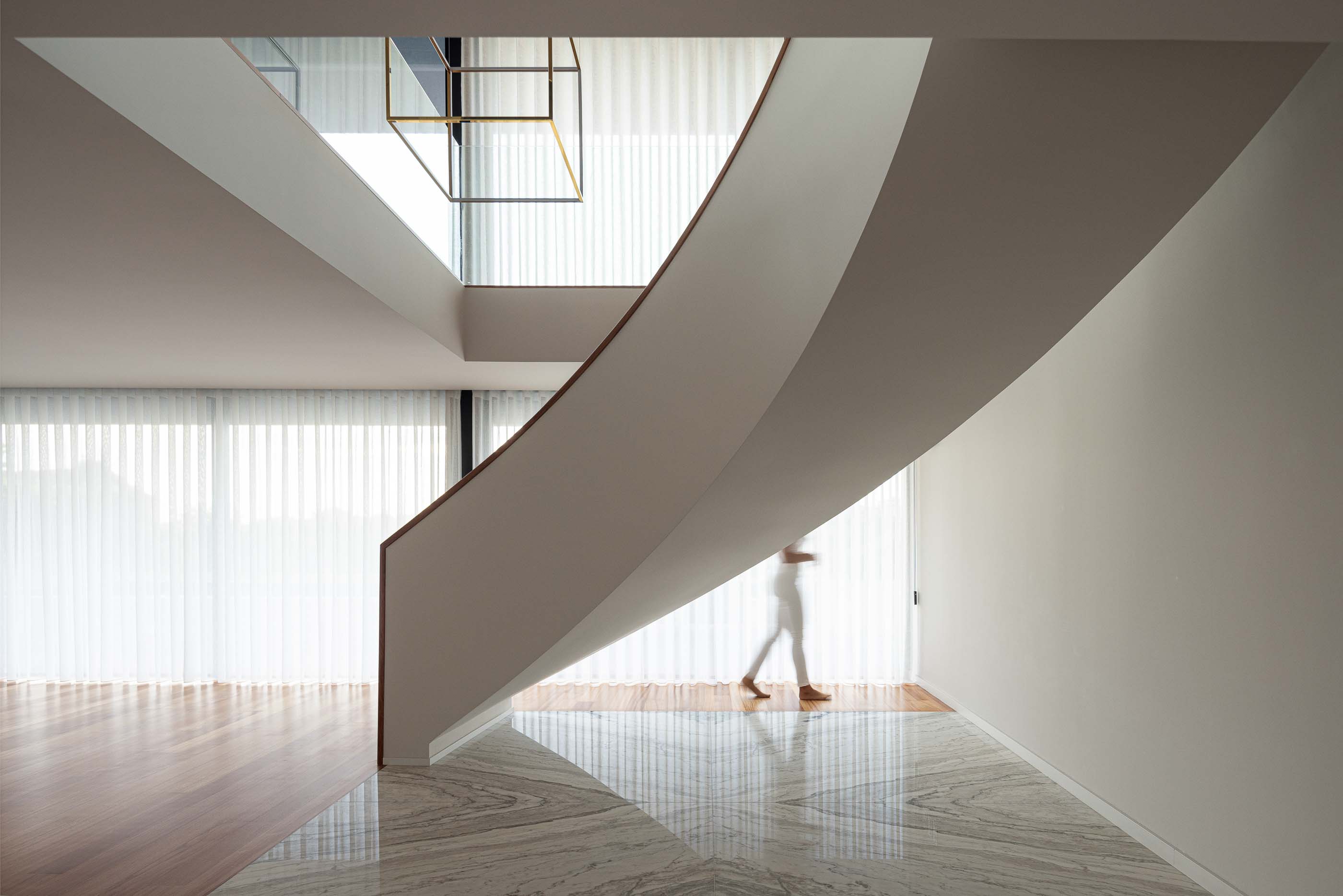 Escadas: Escadas com design moderno, corrimão curvo e candeeiro geométrico suspenso. Pavimento em mármore e madeira. — Casa da Encosta arquitetura Ricardo Azevedo Arquitecto em Santo Tirso