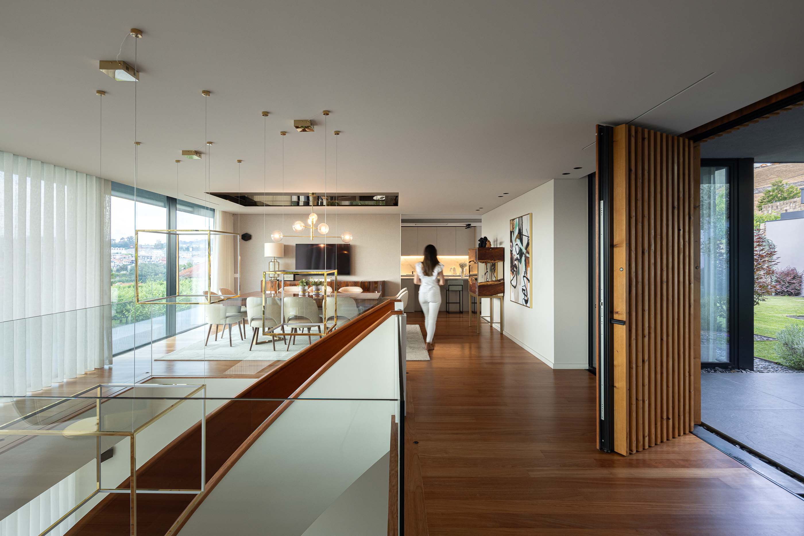 Sala de estar/Jantar: Vista da sala de estar e jantar a partir do topo das escadas, com mesa de jantar, cadeiras e vista para o exterior. — Casa da Encosta arquitetura Ricardo Azevedo Arquitecto em Santo Tirso