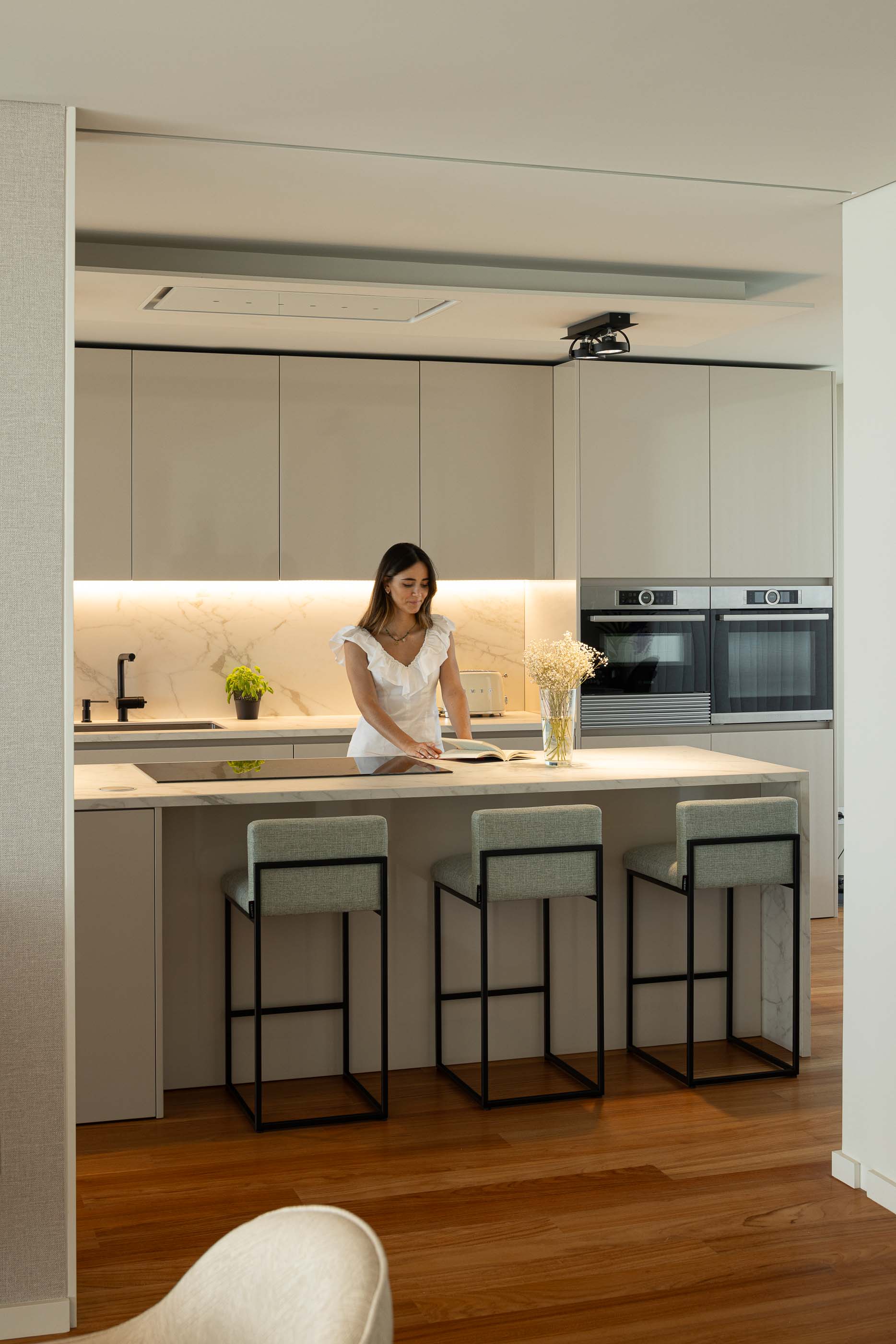 Cozinha: Cozinha com armários brancos, bancada em mármore, cadeiras altas e pavimento em madeira. Design moderno e funcional. — Casa da Encosta arquitetura Ricardo Azevedo Arquitecto em Santo Tirso