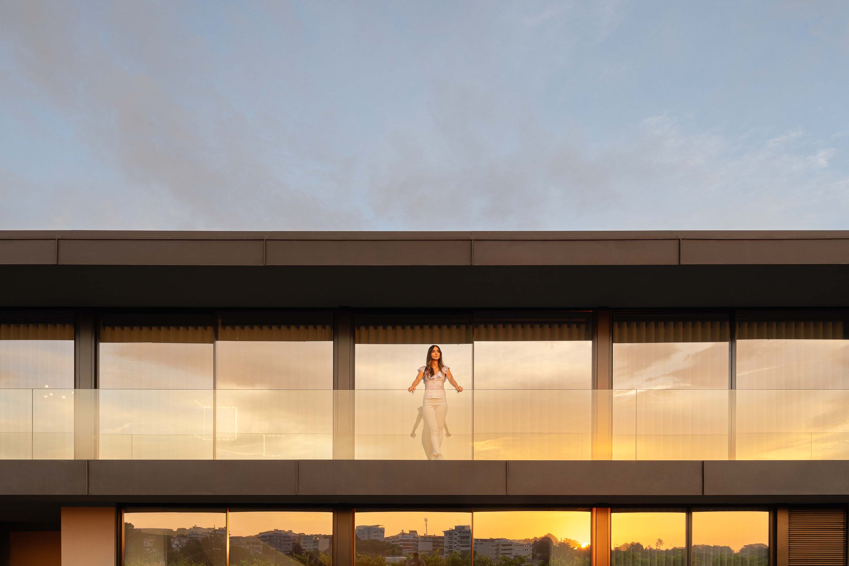 Exterior: Fachada da casa com varanda e grandes janelas, ao pôr do sol. Arquitetura moderna com linhas retas. — Casa da Encosta arquitetura Ricardo Azevedo Arquitecto em Santo Tirso