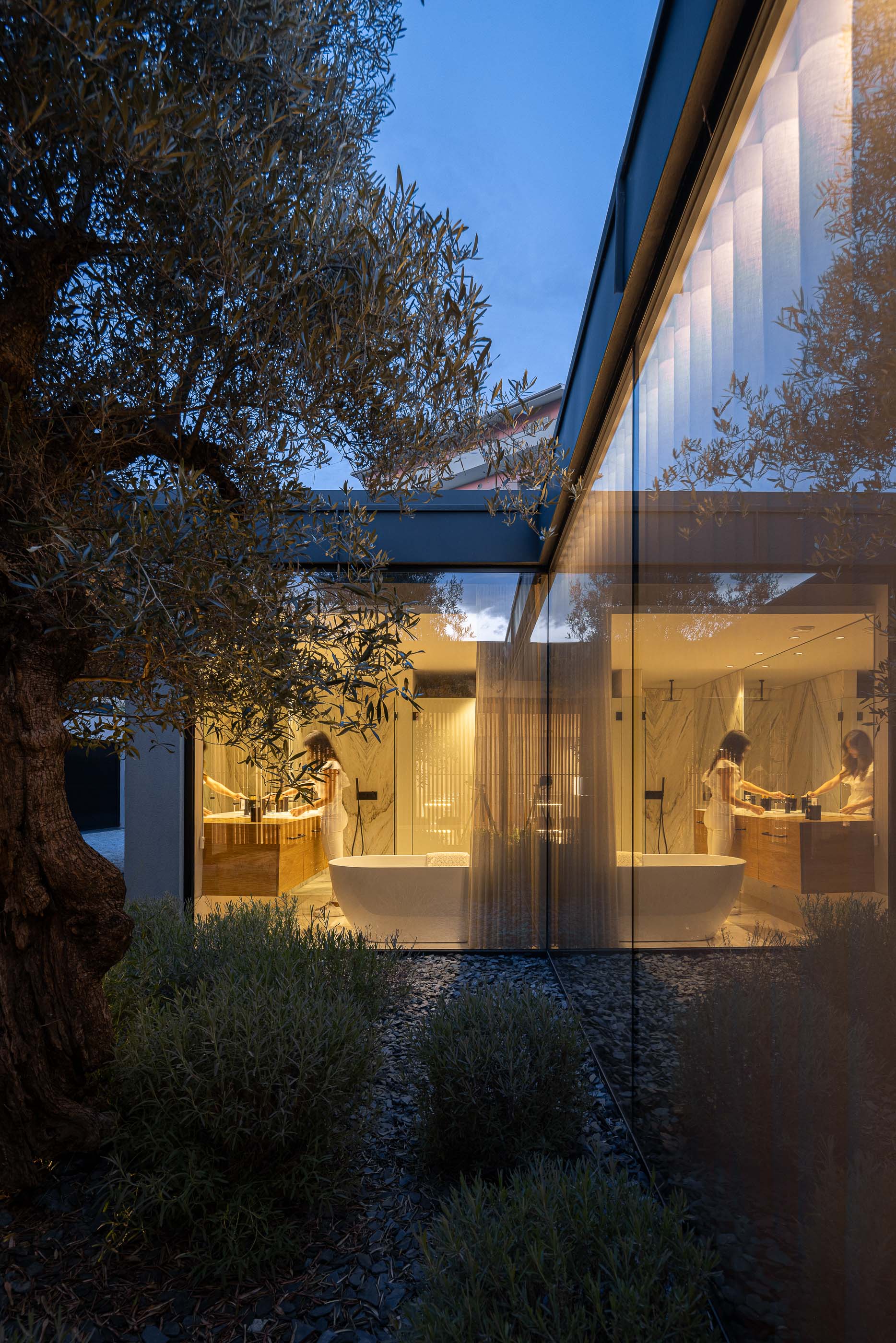 Casa de banho: Vista da casa de banho com banheira, lavatórios e pátio interior com oliveira. Design moderno e relaxante. — Casa da Encosta arquitetura Ricardo Azevedo Arquitecto em Santo Tirso