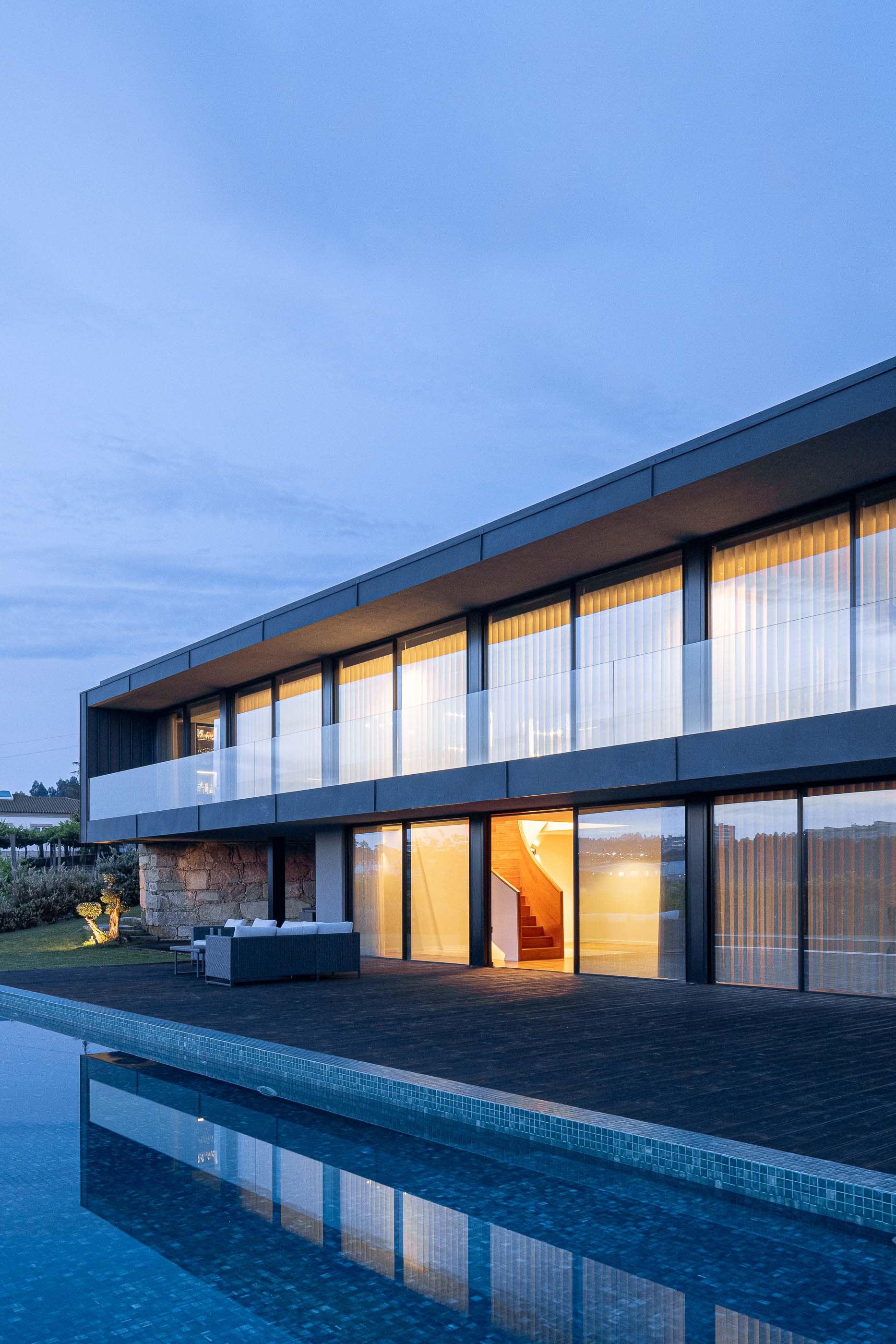Exterior: Vista da piscina, zona de estar exterior e fachada da casa com grandes janelas. Arquitetura moderna e minimalista. — Casa da Encosta arquitetura Ricardo Azevedo Arquitecto em Santo Tirso