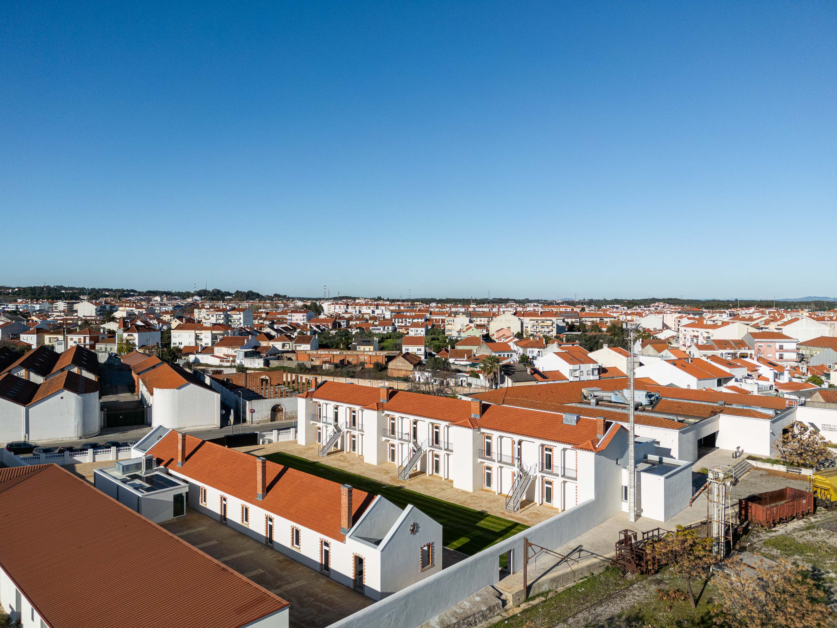 Vista aérea: Conjunto habitacional branco com telhados vermelhos, integrado na malha urbana da cidade do Entroncamento. — Reabilitação Urbana do Bairro do Boneco arquitetura Adarq - André David Arquitecto em Entroncamento