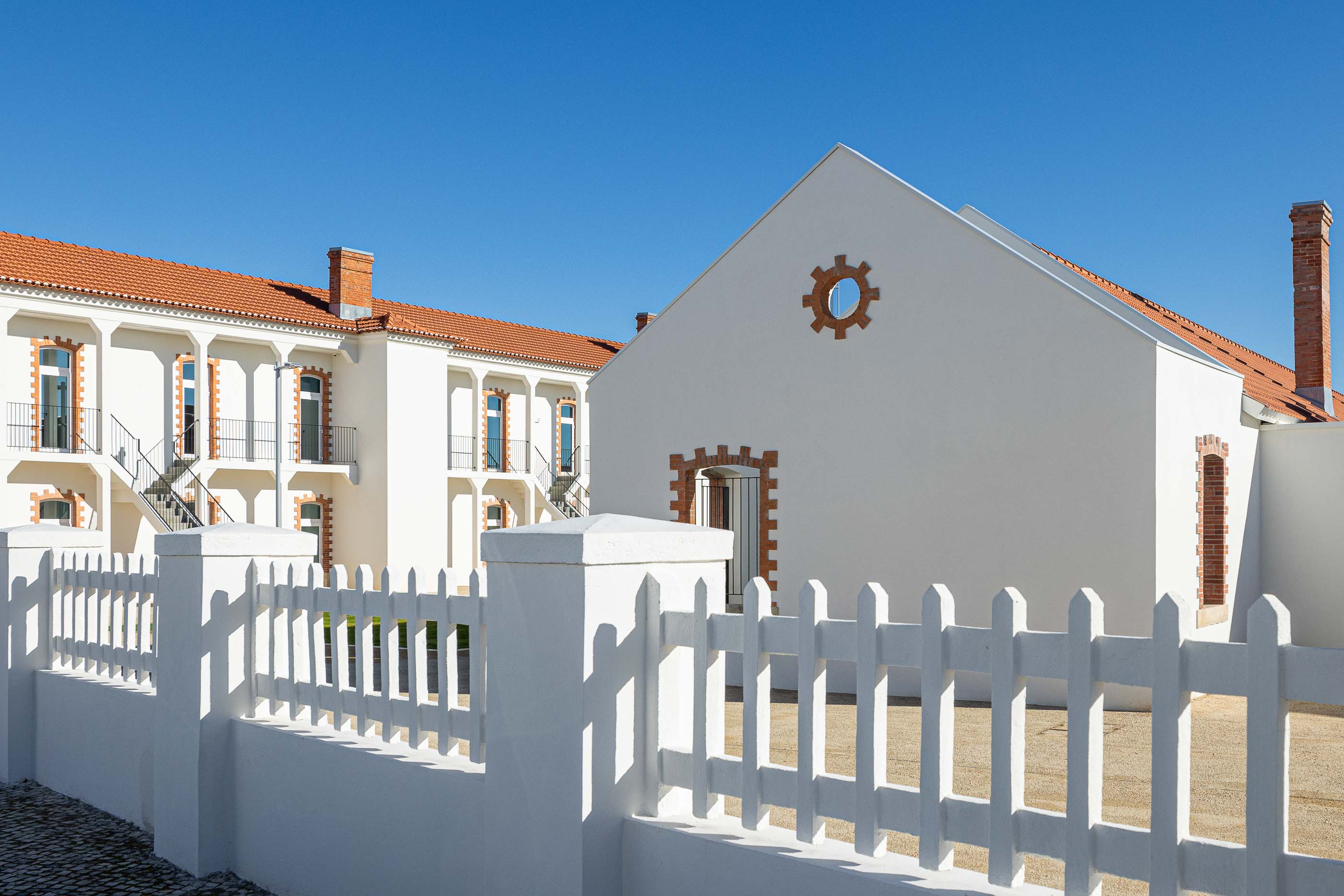 Exterior: Edifício branco com detalhes em tijolo, telhado cerâmico e vedação branca em madeira. — Reabilitação Urbana do Bairro do Boneco arquitetura Adarq - André David Arquitecto em Entroncamento