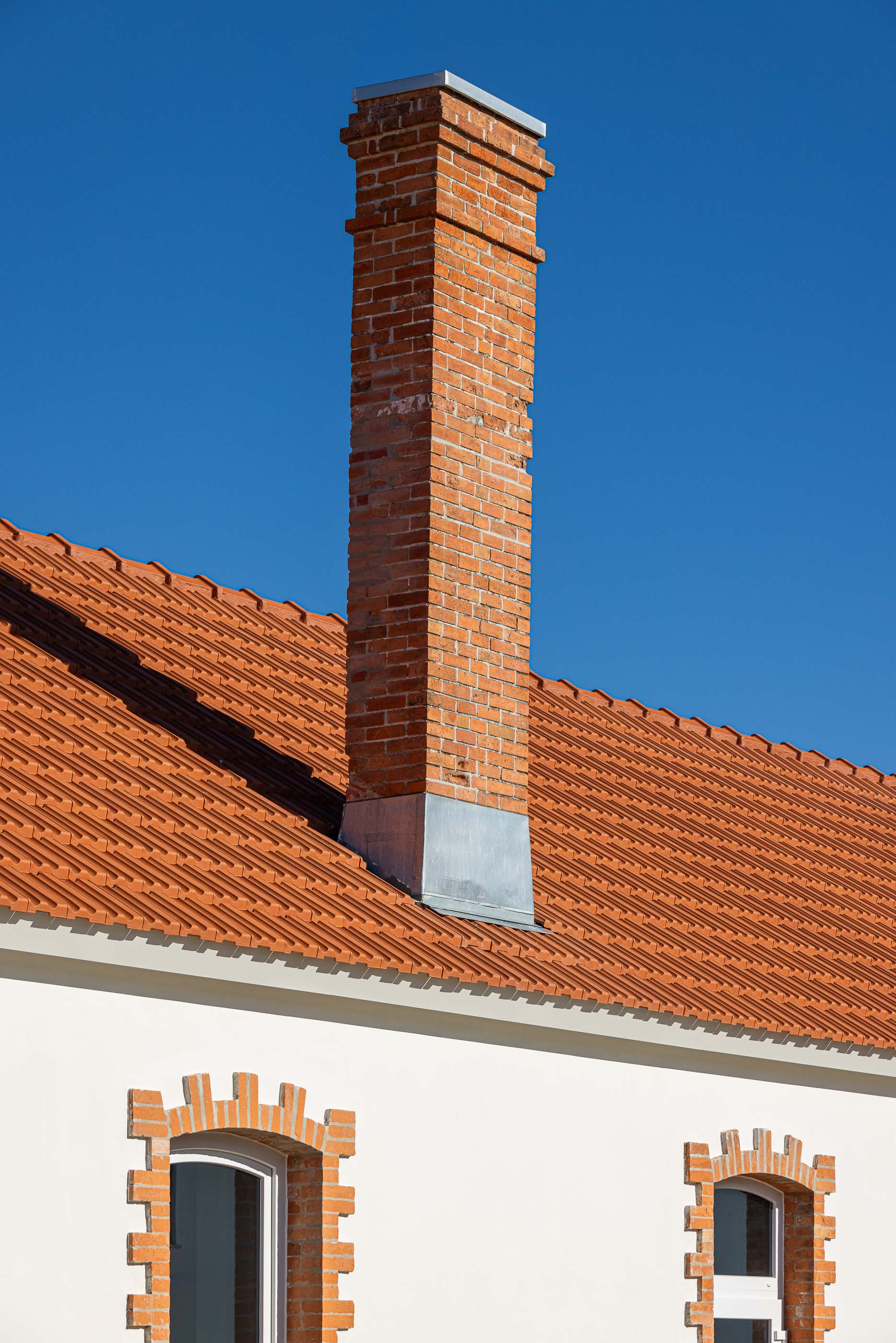 Detalhe: Chaminé em tijolo sobre telhado cerâmico, com janelas emolduradas em tijolo aparente. — Reabilitação Urbana do Bairro do Boneco arquitetura Adarq - André David Arquitecto em Entroncamento