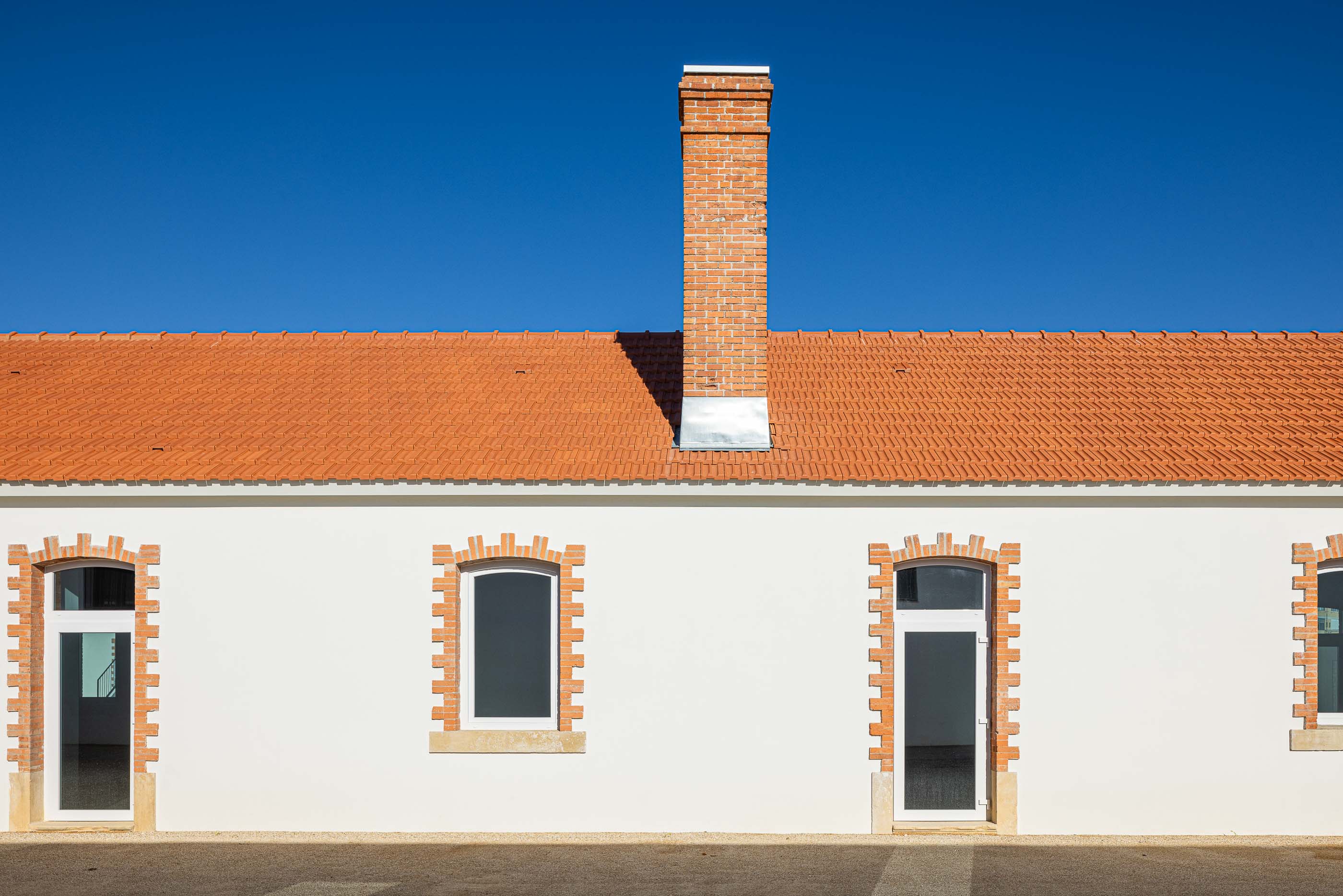 Exterior: Fachada branca com telhado cerâmico e chaminé em tijolo, janelas e portas emolduradas a tijolo. — Reabilitação Urbana do Bairro do Boneco arquitetura Adarq - André David Arquitecto em Entroncamento