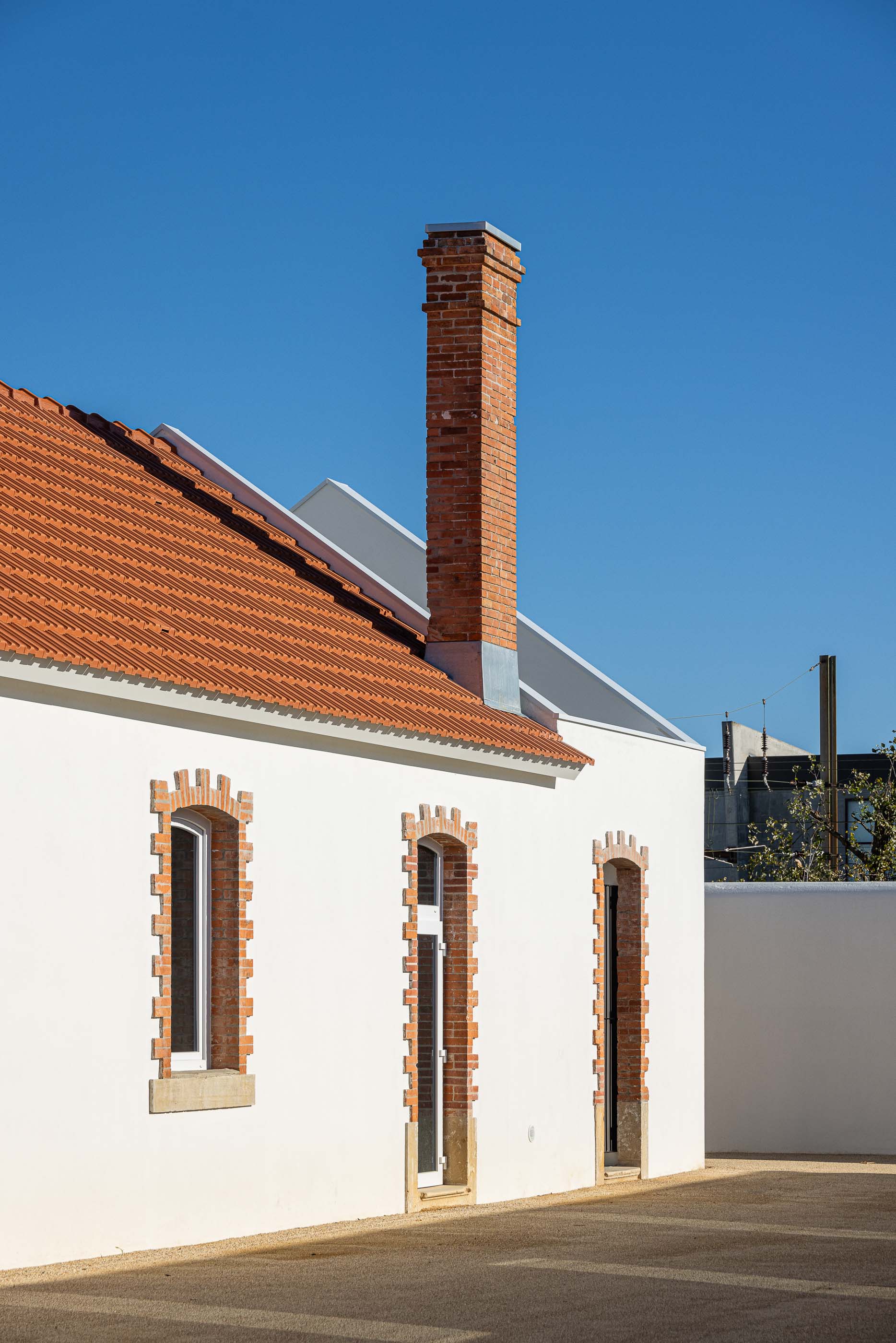 Exterior: Edifício branco com telhado cerâmico e chaminé em tijolo, janelas emolduradas a tijolo aparente. — Reabilitação Urbana do Bairro do Boneco arquitetura Adarq - André David Arquitecto em Entroncamento