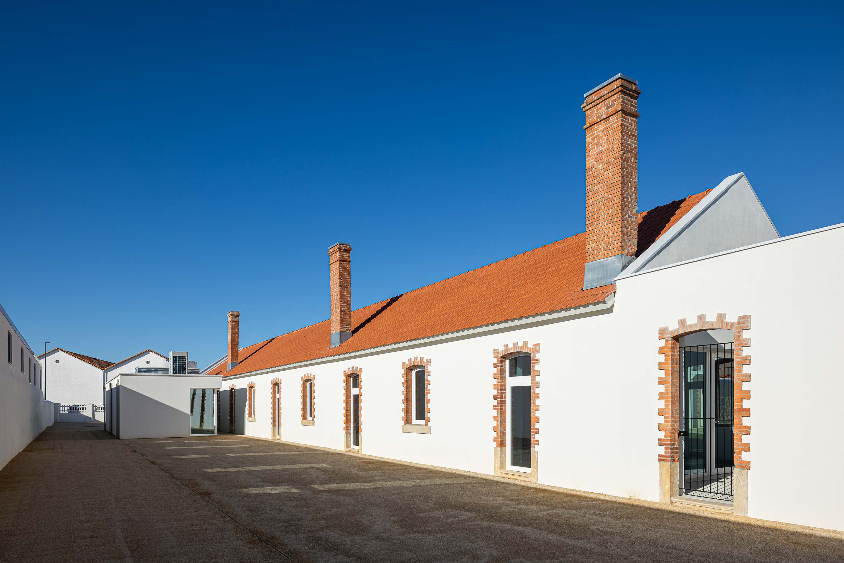 Exterior: Edifícios brancos com telhado cerâmico, chaminés em tijolo e pátio com gravilha. — Reabilitação Urbana do Bairro do Boneco arquitetura Adarq - André David Arquitecto em Entroncamento
