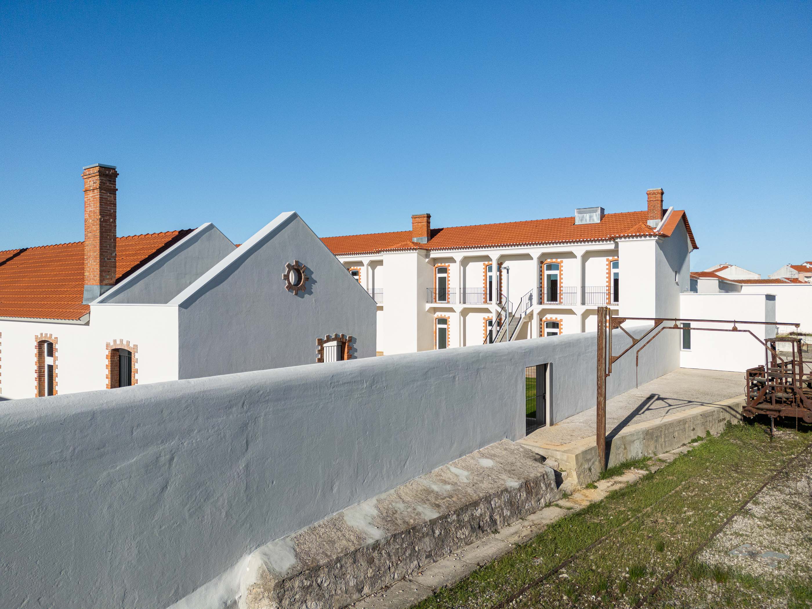 Exterior: Edifícios brancos com telhado cerâmico, pátio e elementos ferroviários antigos. — Reabilitação Urbana do Bairro do Boneco arquitetura Adarq - André David Arquitecto em Entroncamento