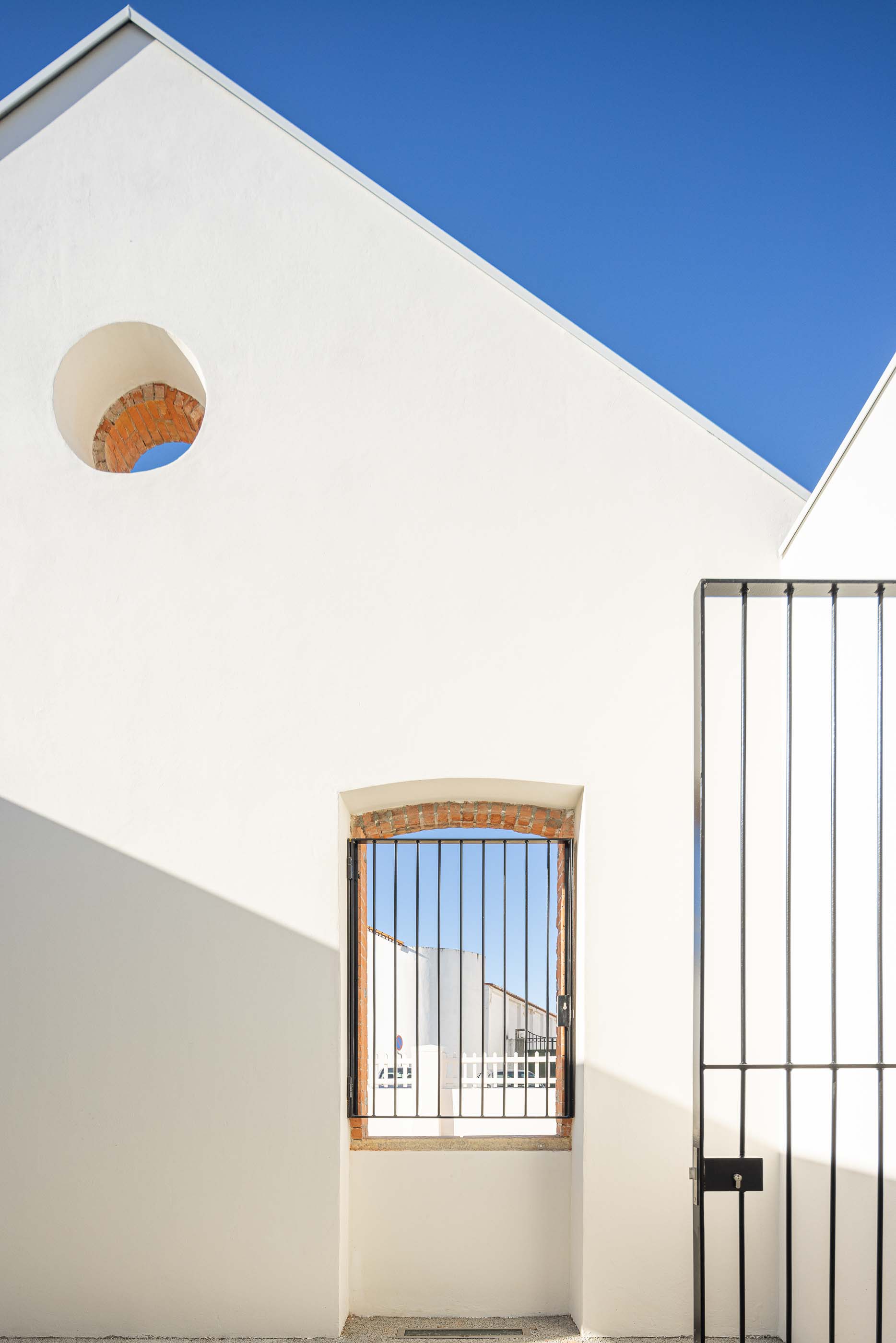 Exterior: Detalhe de fachada branca com janelas gradeadas e óculo circular em tijolo aparente. — Reabilitação Urbana do Bairro do Boneco arquitetura Adarq - André David Arquitecto em Entroncamento