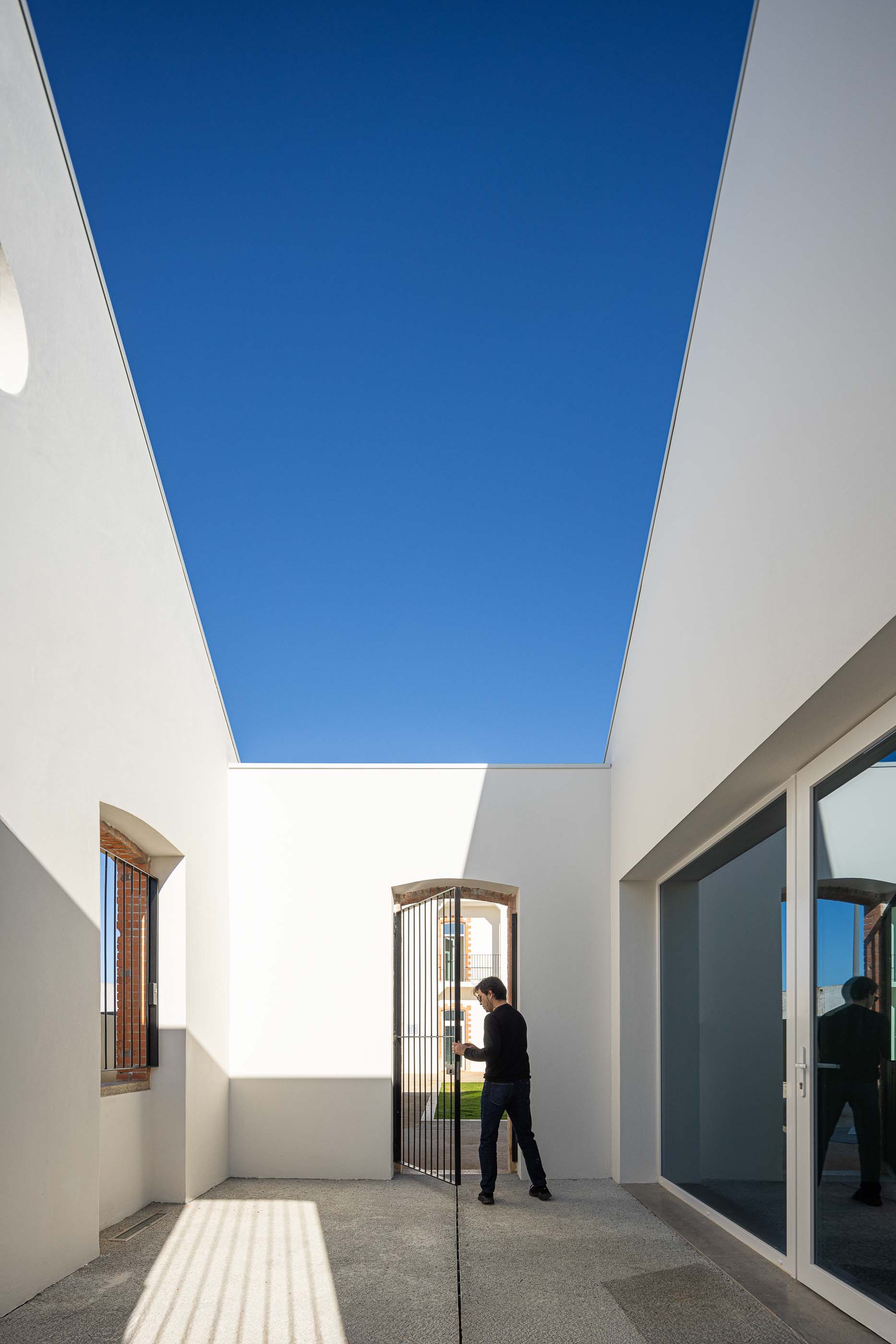 Pátio interior: Espaço exterior delimitado por paredes brancas, com portão gradeado e pavimento em betão. — Reabilitação Urbana do Bairro do Boneco arquitetura Adarq - André David Arquitecto em Entroncamento