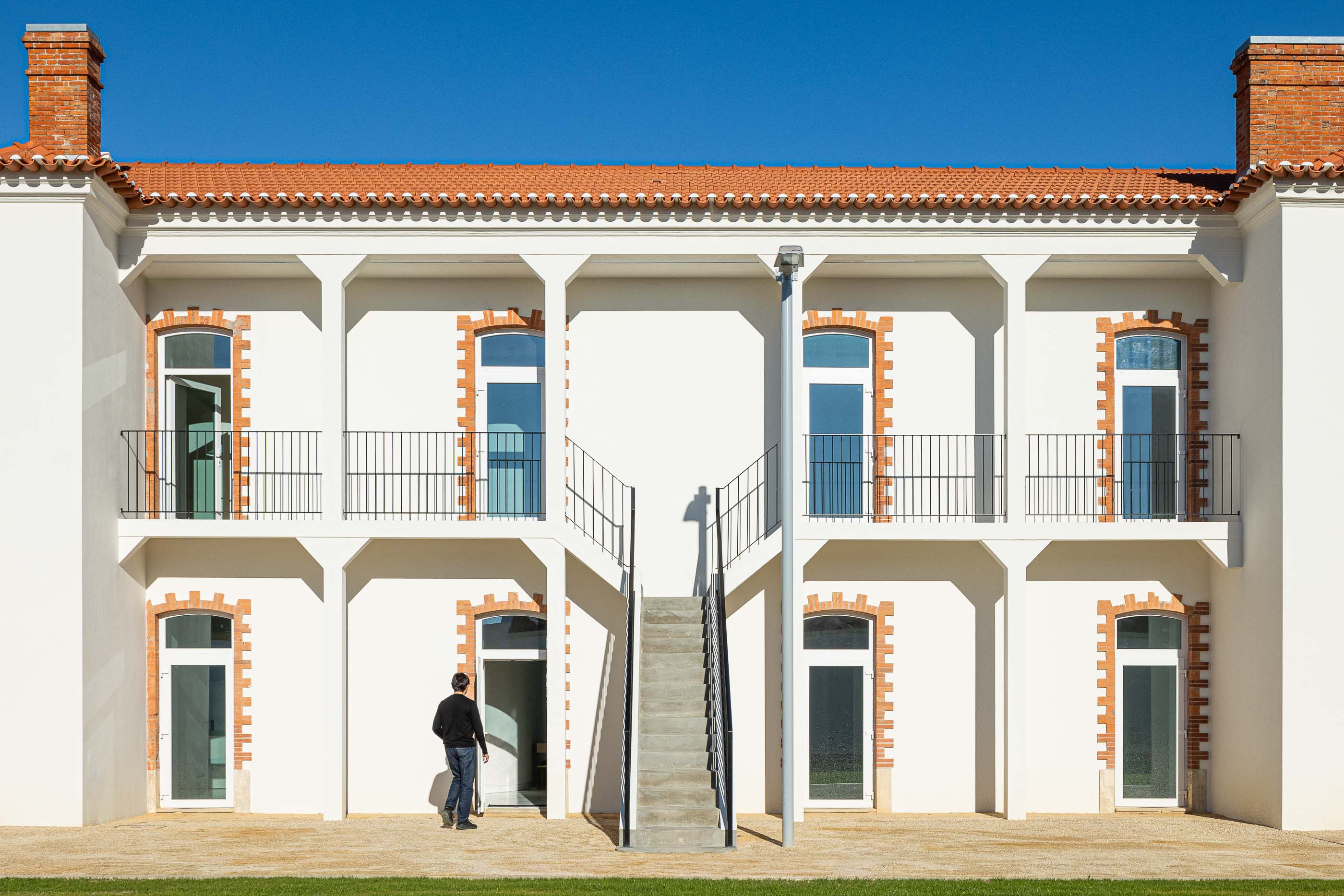 Exterior: Fachada de edifício branco com colunas, varandas em ferro e escadas de acesso aos pisos superiores. — Reabilitação Urbana do Bairro do Boneco arquitetura Adarq - André David Arquitecto em Entroncamento