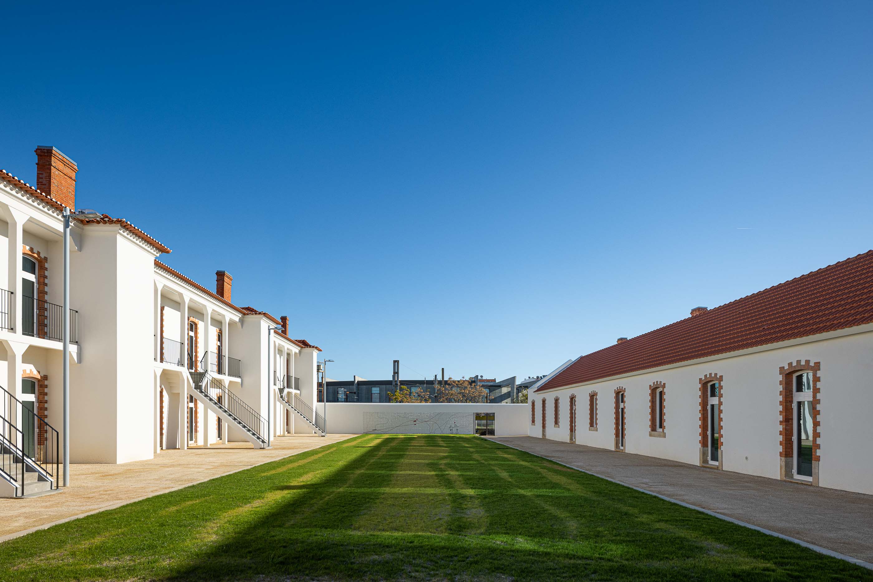 Exterior: Edifícios brancos com telhado cerâmico, escadas de acesso e relvado central. — Reabilitação Urbana do Bairro do Boneco arquitetura Adarq - André David Arquitecto em Entroncamento