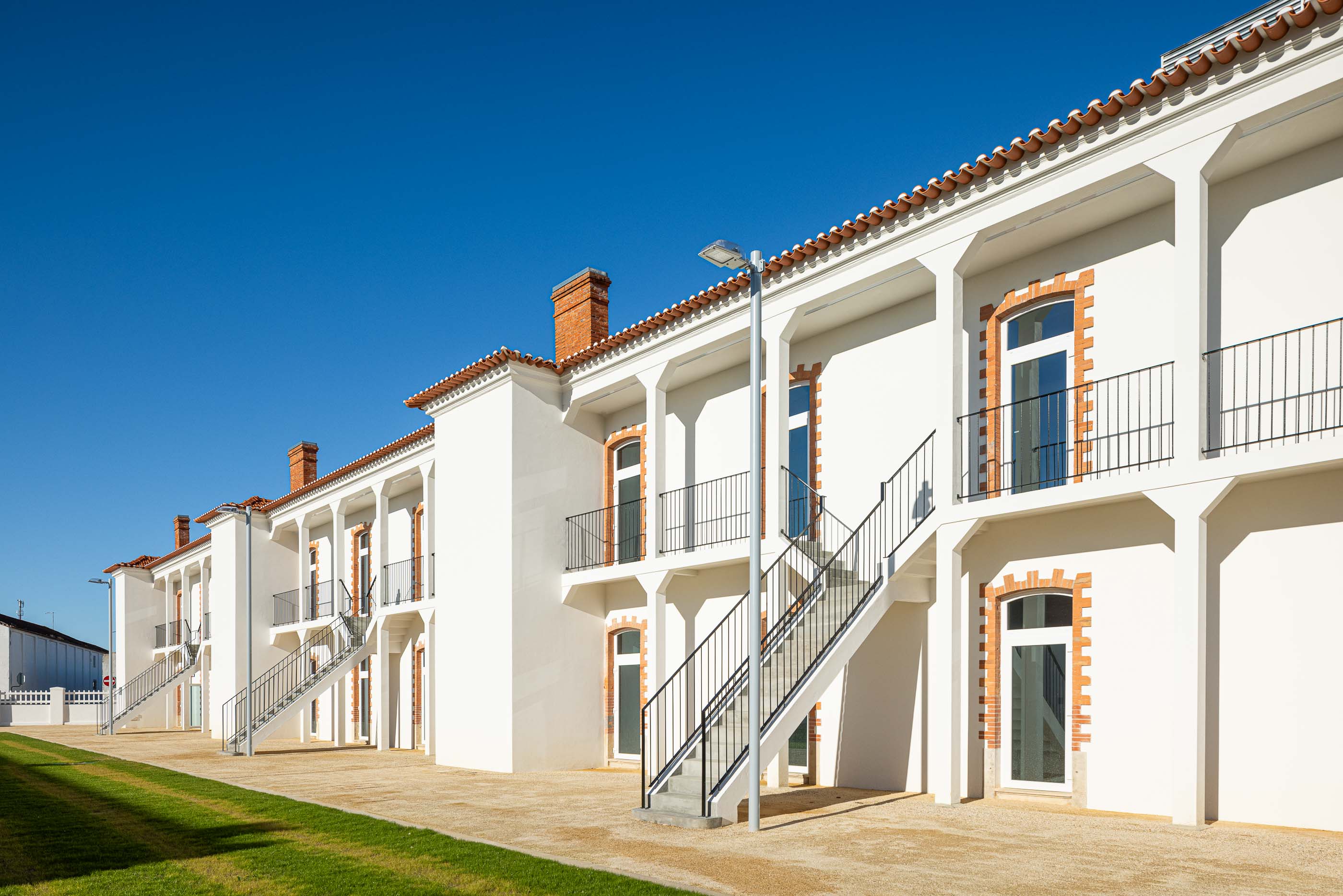 Exterior: Edifício branco com colunas, varandas em ferro e escadas de acesso aos pisos superiores. — Reabilitação Urbana do Bairro do Boneco arquitetura Adarq - André David Arquitecto em Entroncamento